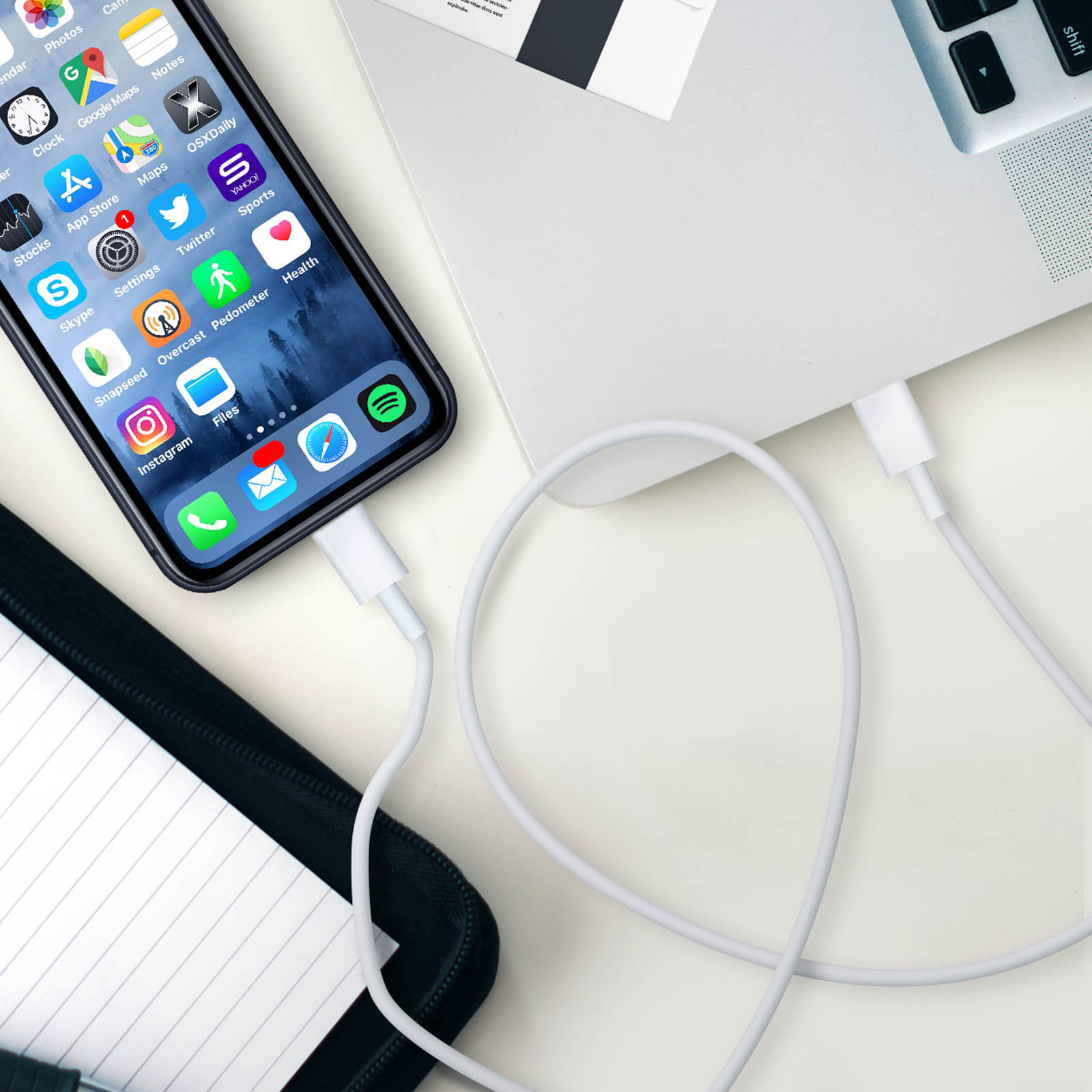 Telefono in carica con cavo bianco collegato a laptop e scrivania.