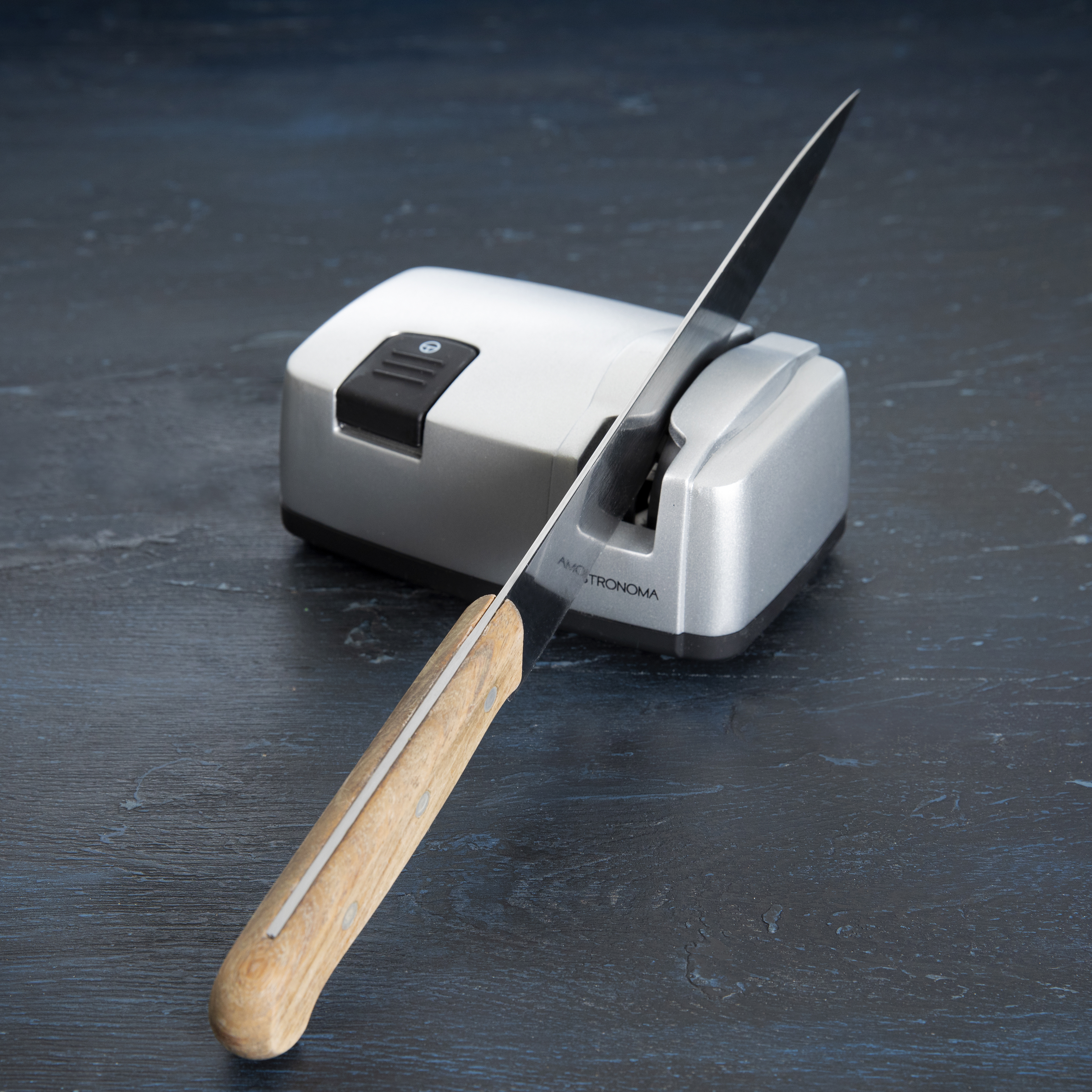 Nóż jest ostrzony na srebrnej ostrzałce do noży na niebieskiej powierzchni.