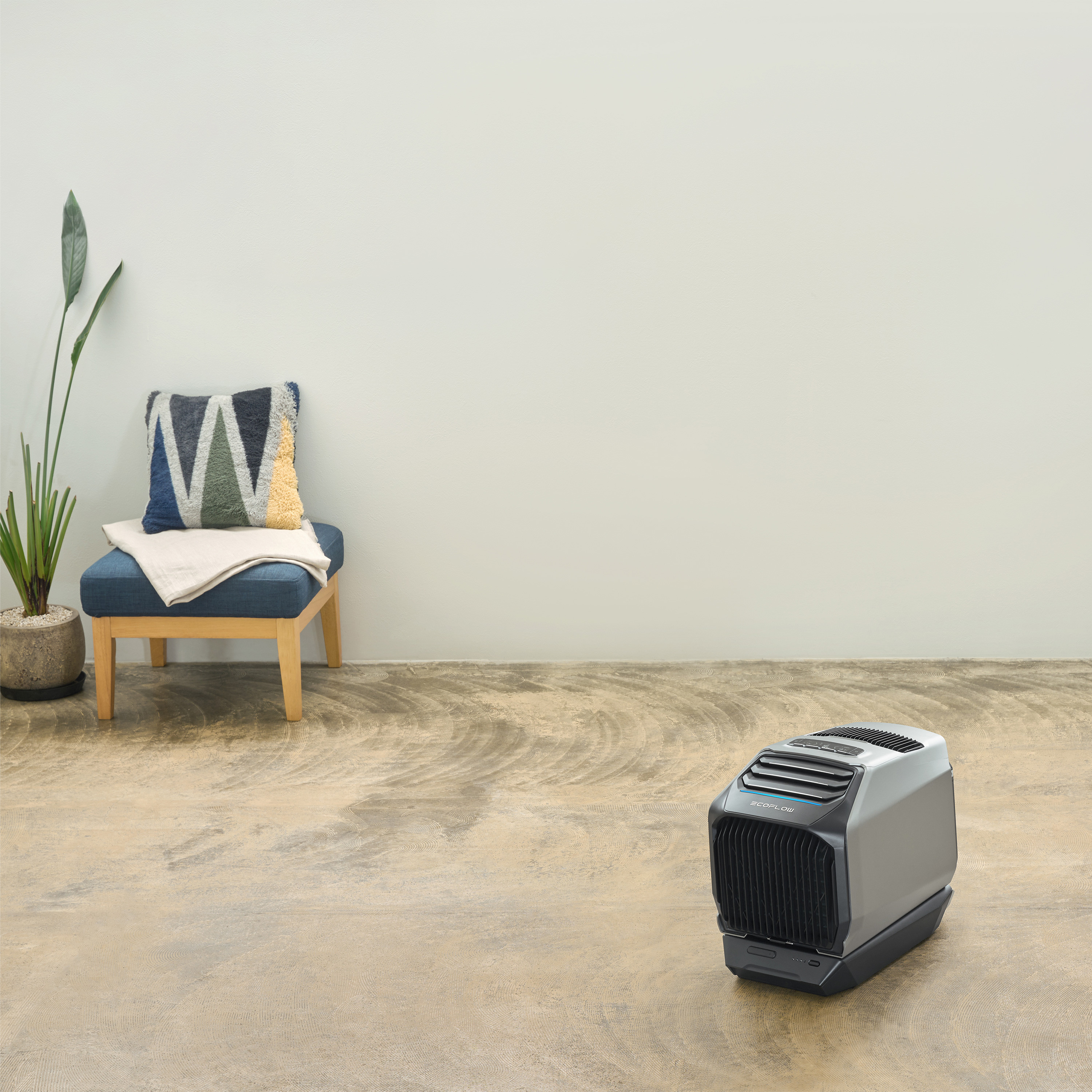 Pokój z wentylatorem, krzesłem z poduszką i małym oczyszczaczem powietrza na podłodze.