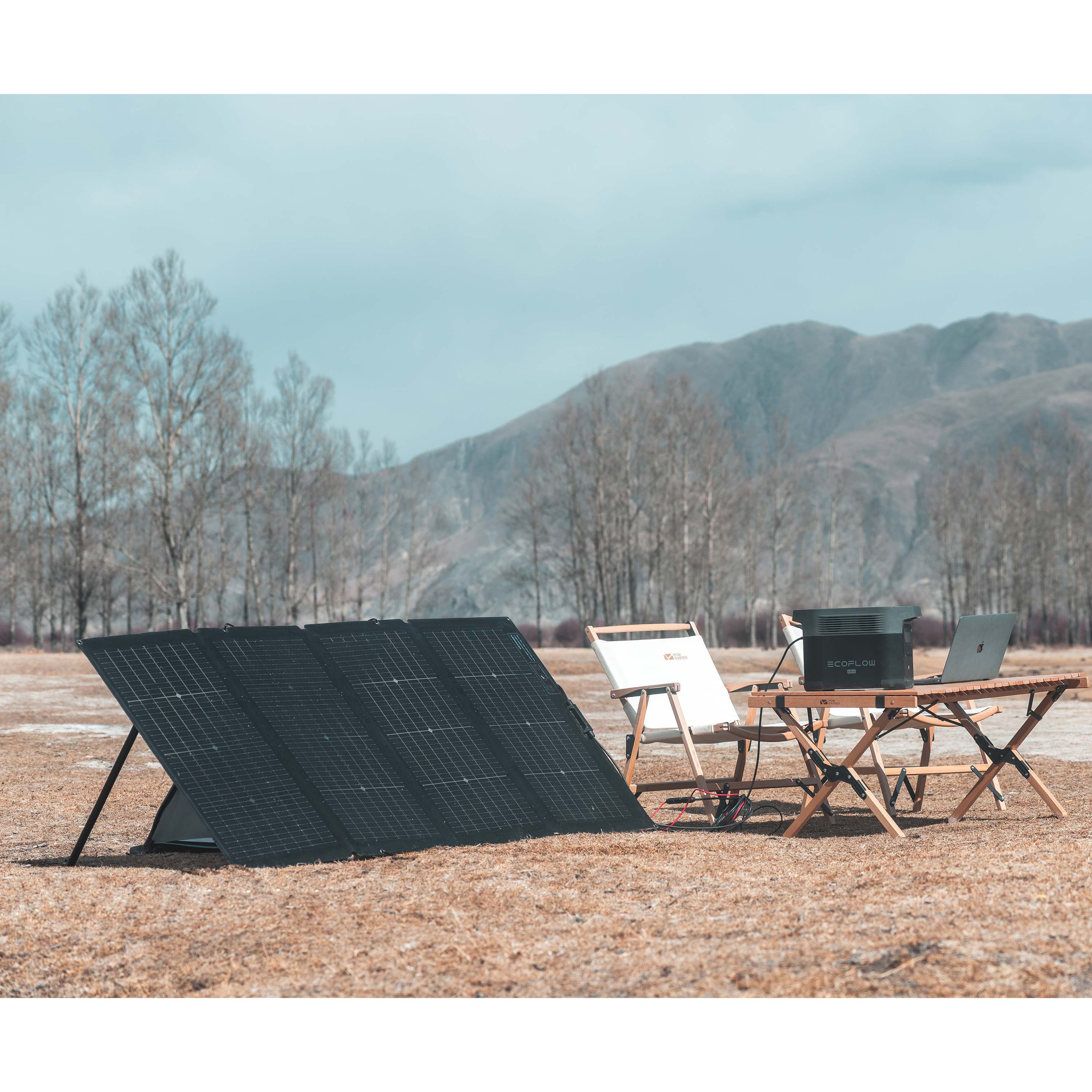Panele słoneczne i sprzęt kempingowy na polu z górami w tle.