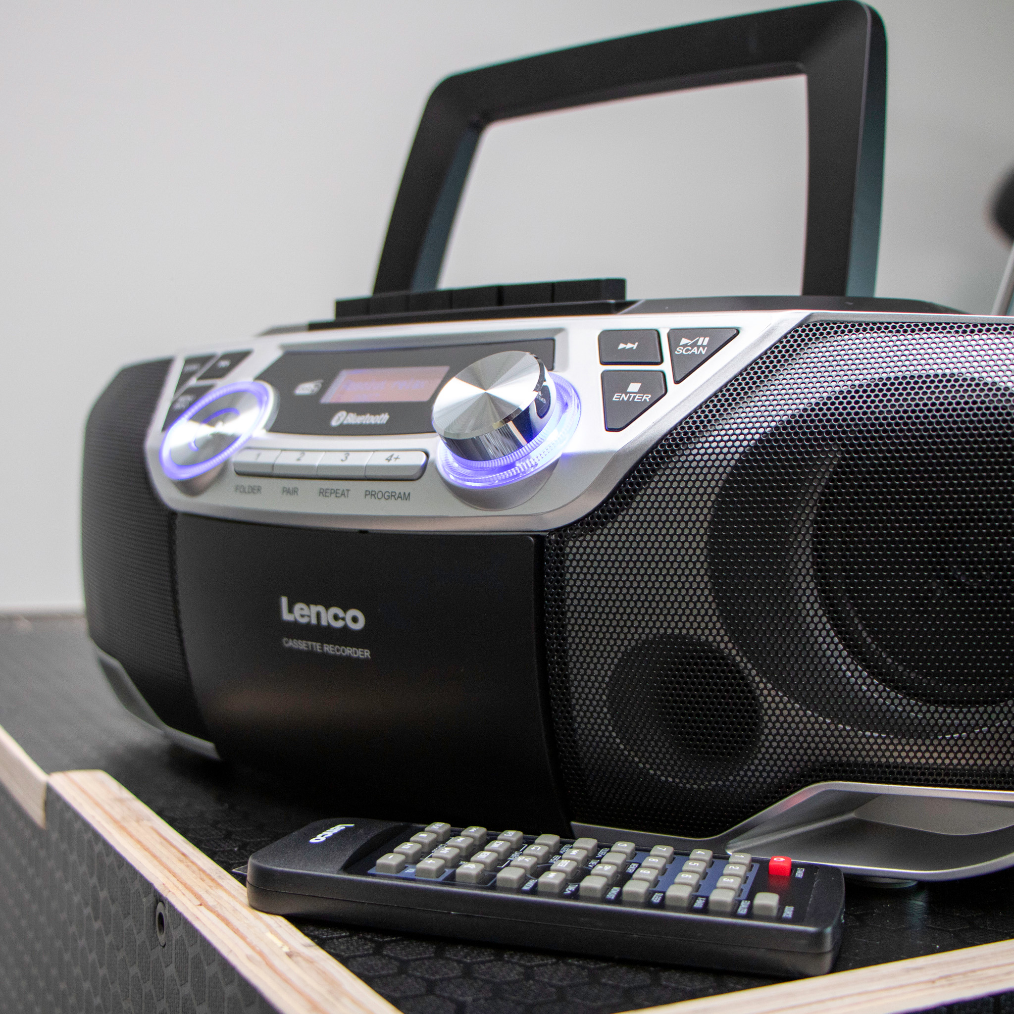 Boombox Lenco noir et argent avec Bluetooth et télécommande sur une surface en bois.