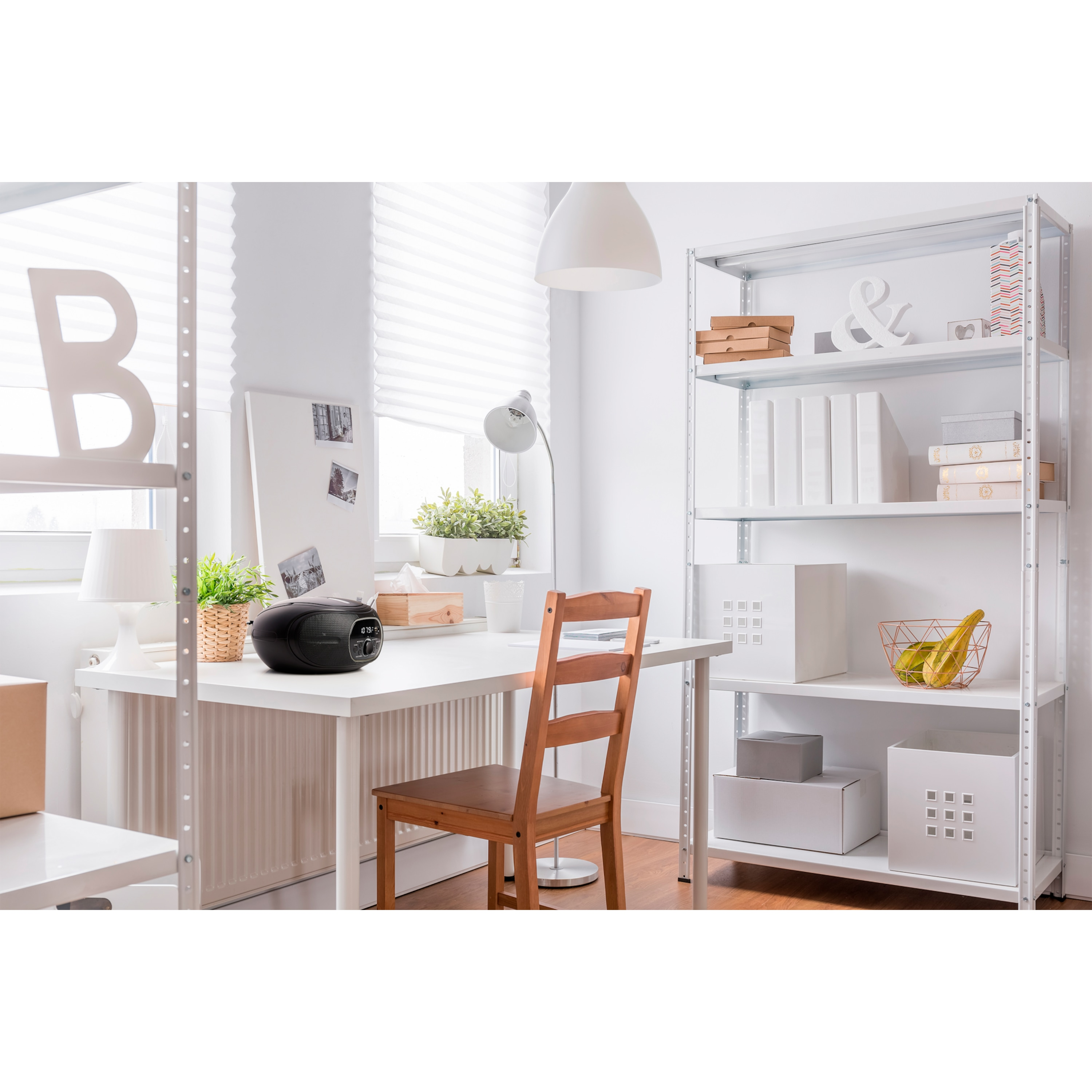 Ein Zimmer mit Schreibtisch, Regalen und einem schwarzen Radio. Es gibt ein Fenster und eine Lampe.
