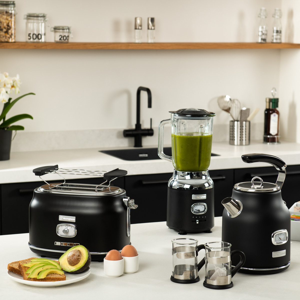 Küchenszene mit Toaster, Mixer mit grüner Flüssigkeit und Wasserkocher auf weißer Oberfläche.