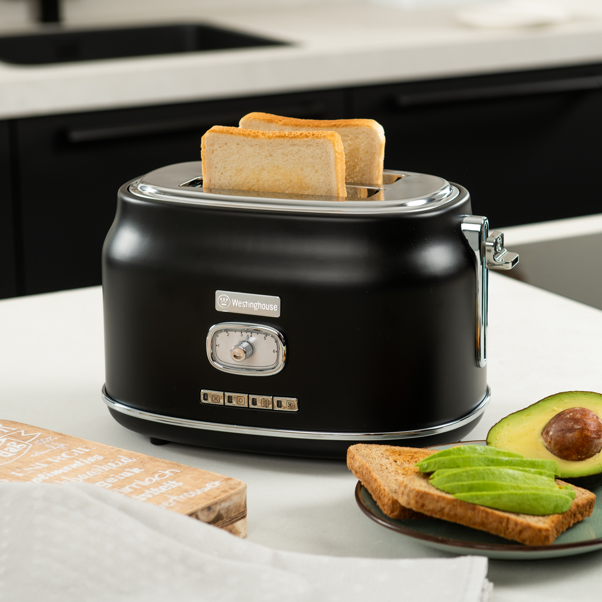 Schwarzer Toaster mit zwei Brotscheiben; Avocado; weißer Tisch; schwarzer Hintergrund.