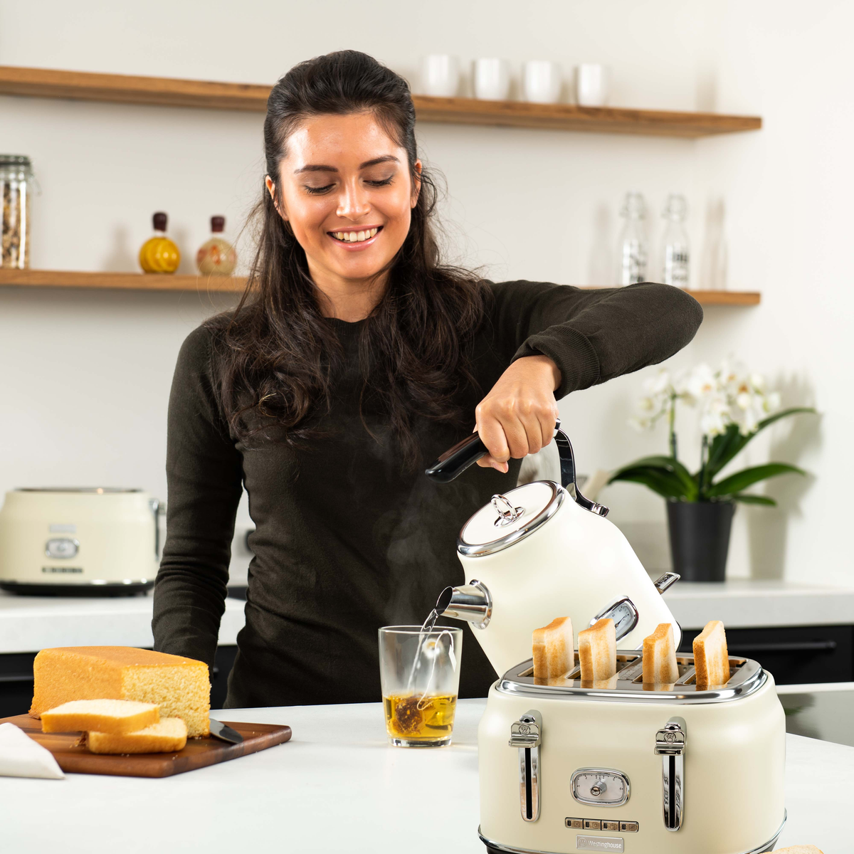 Frau gießt Wasser aus weißem Wasserkocher in ein Glas; Toast und Kuchen.