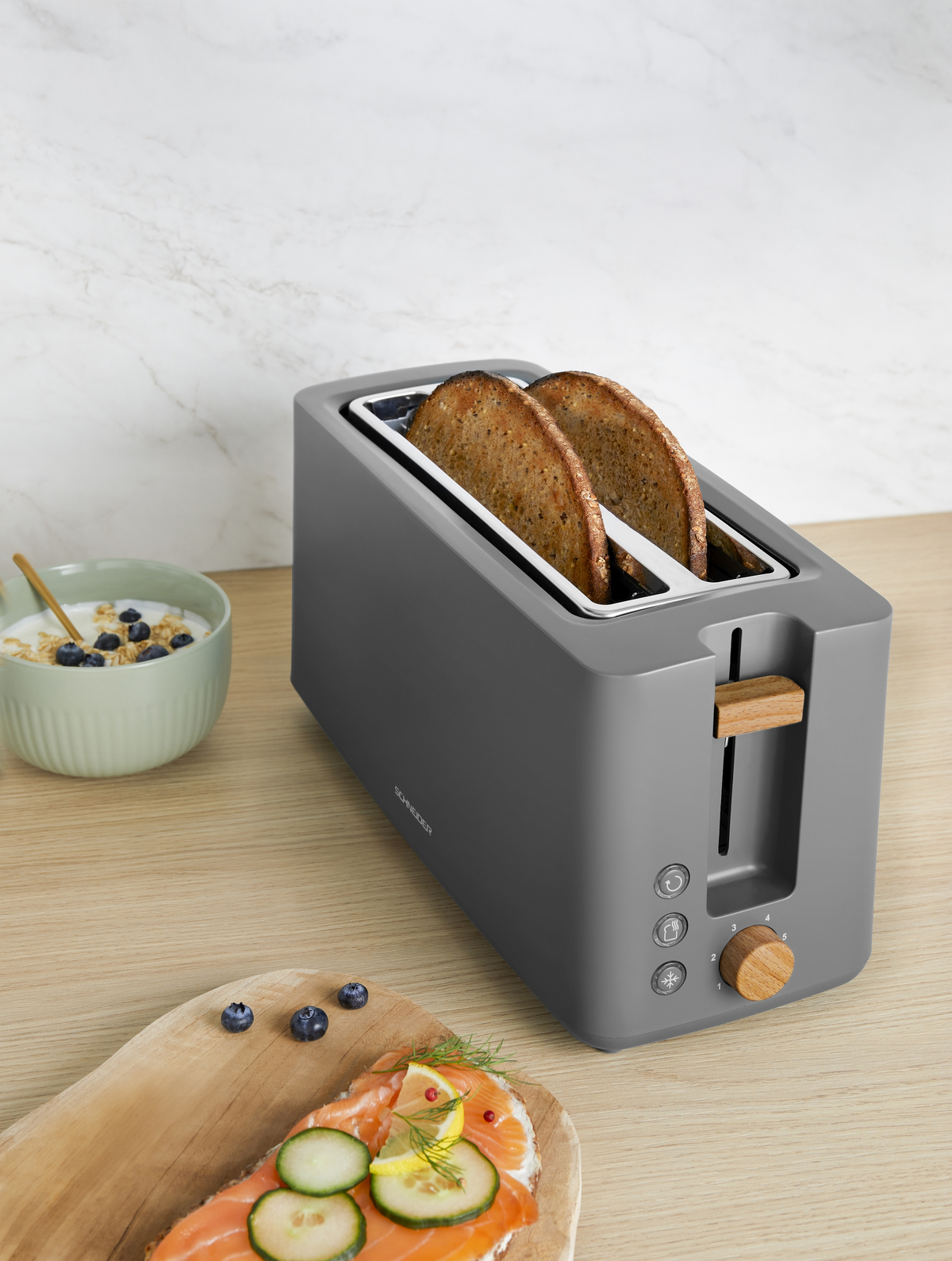 Grauer Toaster mit zwei Toastscheiben, Holzakzenten und Schneidebrett.