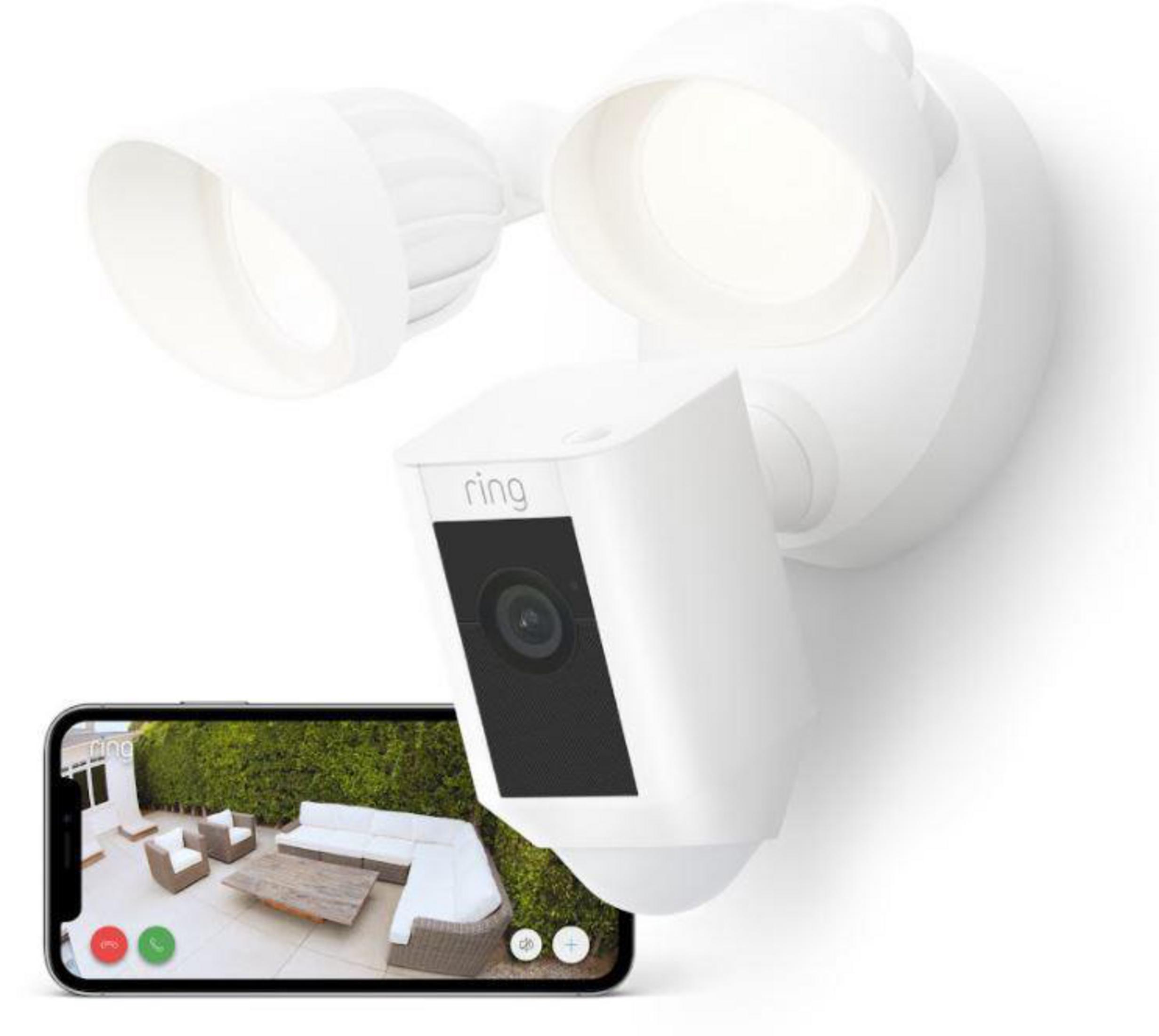 Cámara de seguridad blanca y luces en una pared, con teléfono mostrando una escena al aire libre. Muestra patio y sillas.