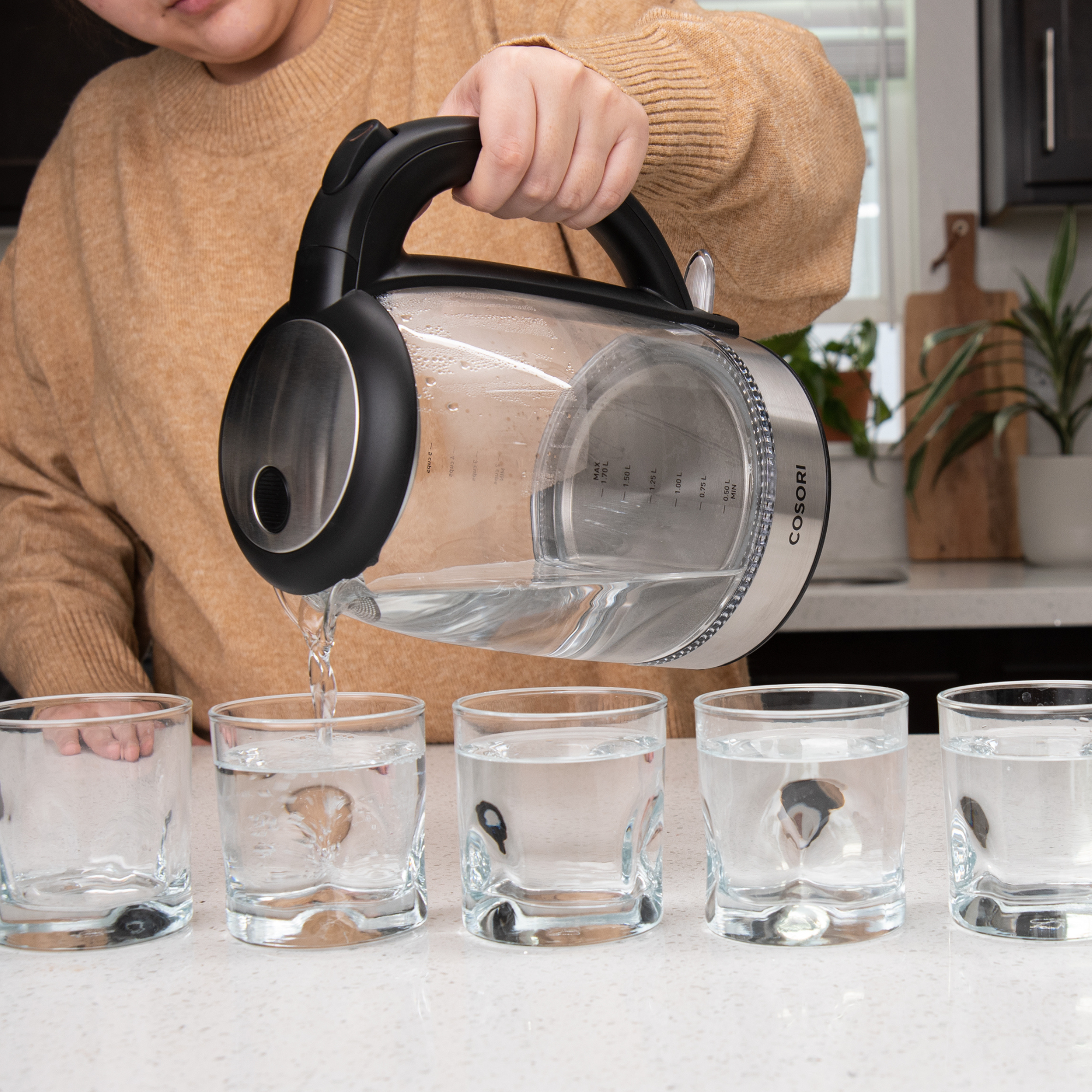 Una persona versa acqua da un bollitore di vetro in cinque bicchieri.