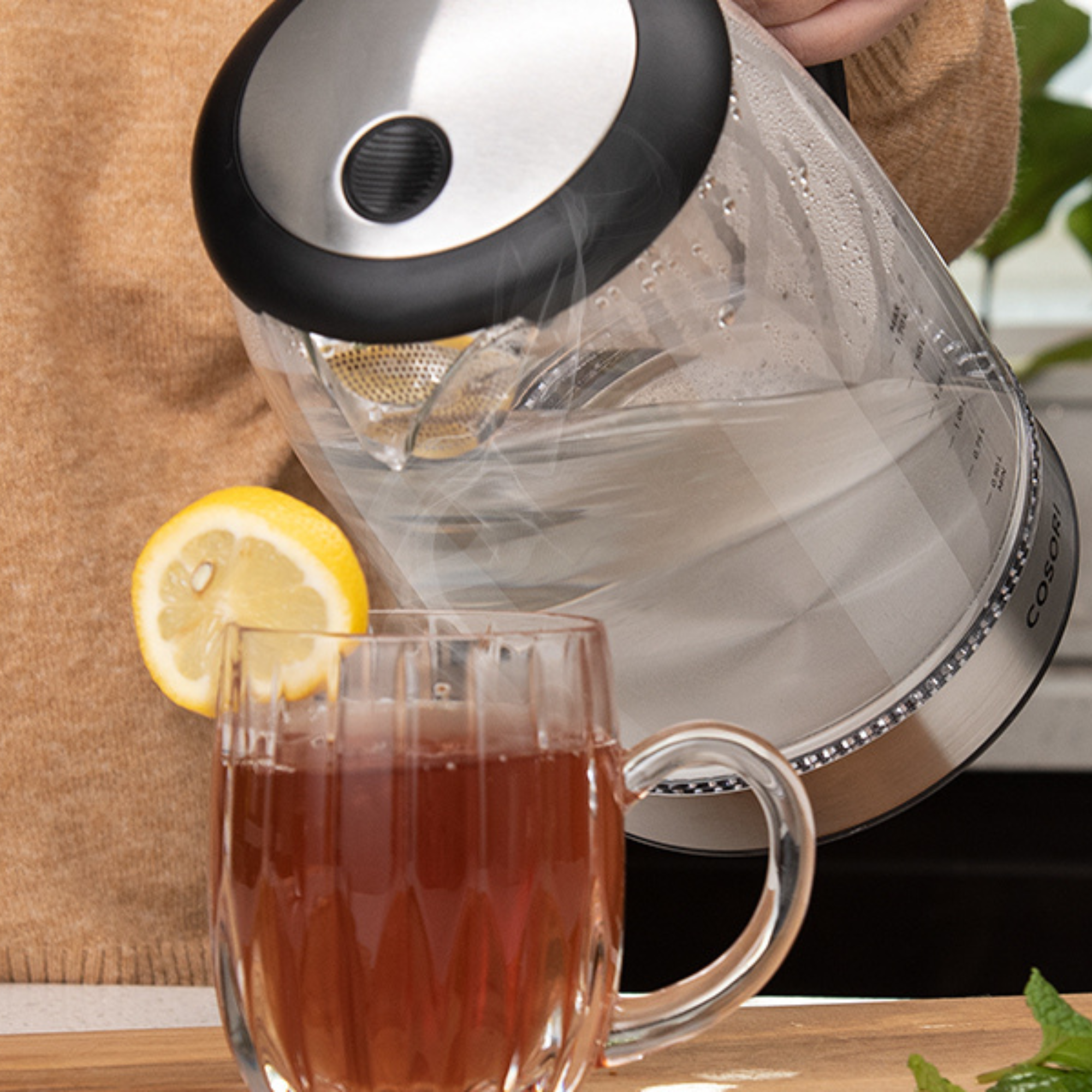 Una persona versa acqua calda da un bollitore di vetro in una tazza di vetro con tè e una fetta di limone.