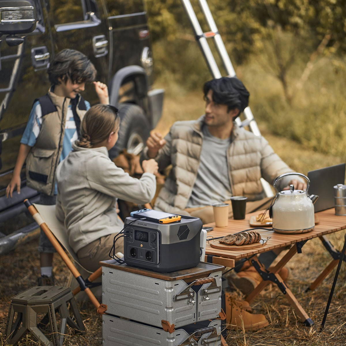 Grupo de personas acampando, con mesa, tetera y estación de energía en la naturaleza.