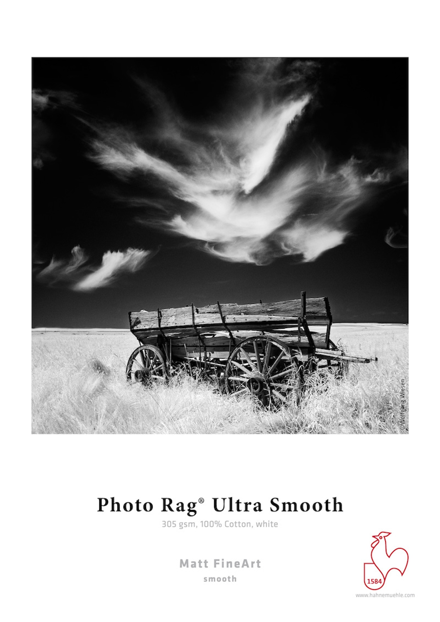 Schwarz-Weiß-Fotografie eines alten Wagens auf einem Feld unter einem bewölkten Himmel.