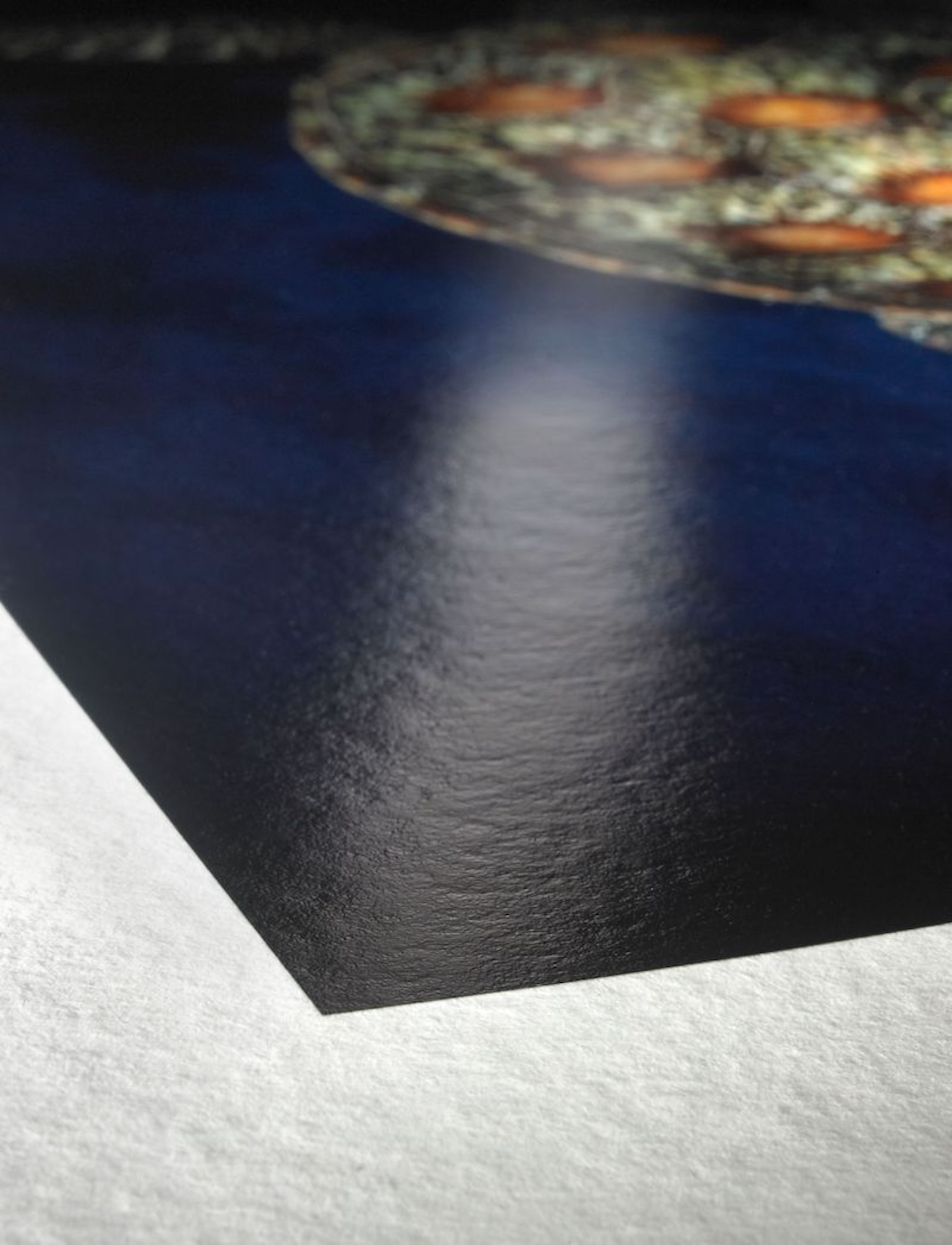 Nahaufnahme einer glänzenden, dunklen Oberfläche. Die Oberfläche reflektiert Licht, mit verschwommenem Hintergrund.