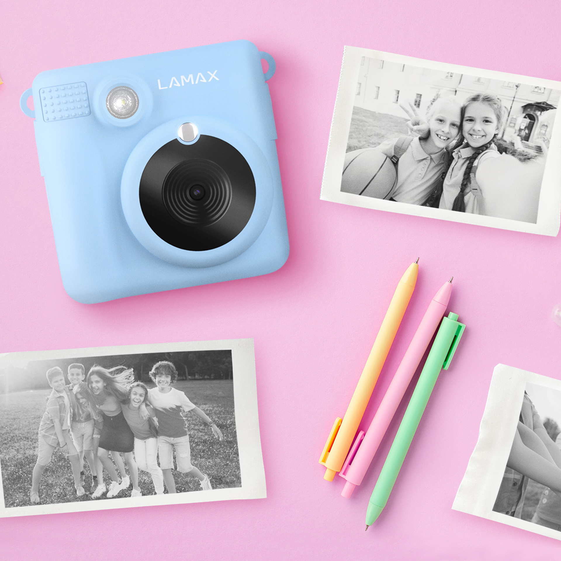 Eine blaue Sofortbildkamera mit Fotos, Stiften und einem rosa Hintergrund.