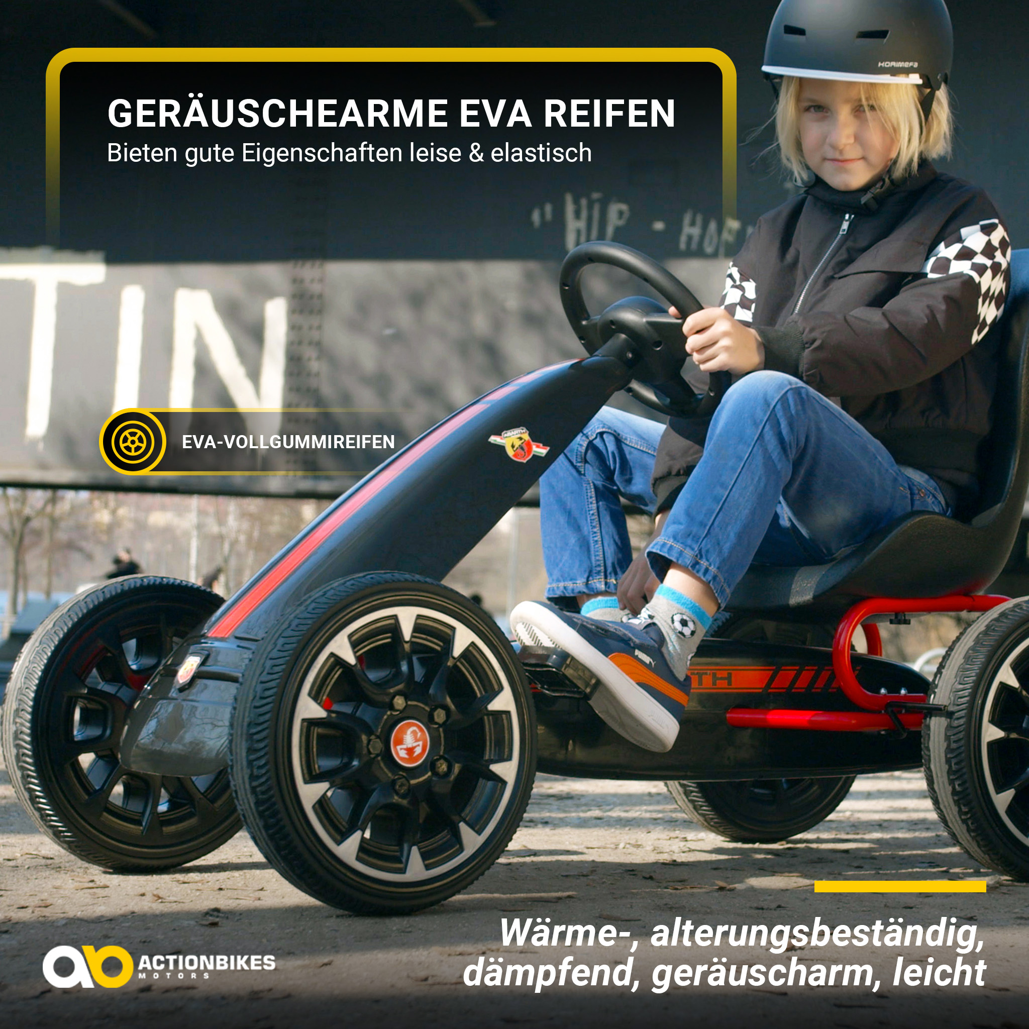 Ein Kind fährt mit einem Kart. Das Kart ist schwarz und rot mit schwarzen Rädern. Das Kind trägt einen Helm.