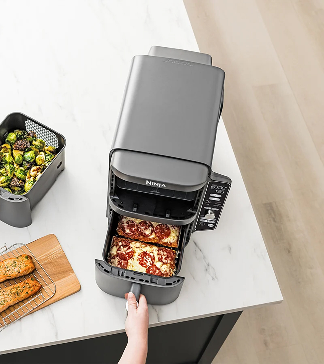 Frytkownica powietrzna z dwoma przegródkami. Jedna z pizzą, druga z brukselką i łososiem.