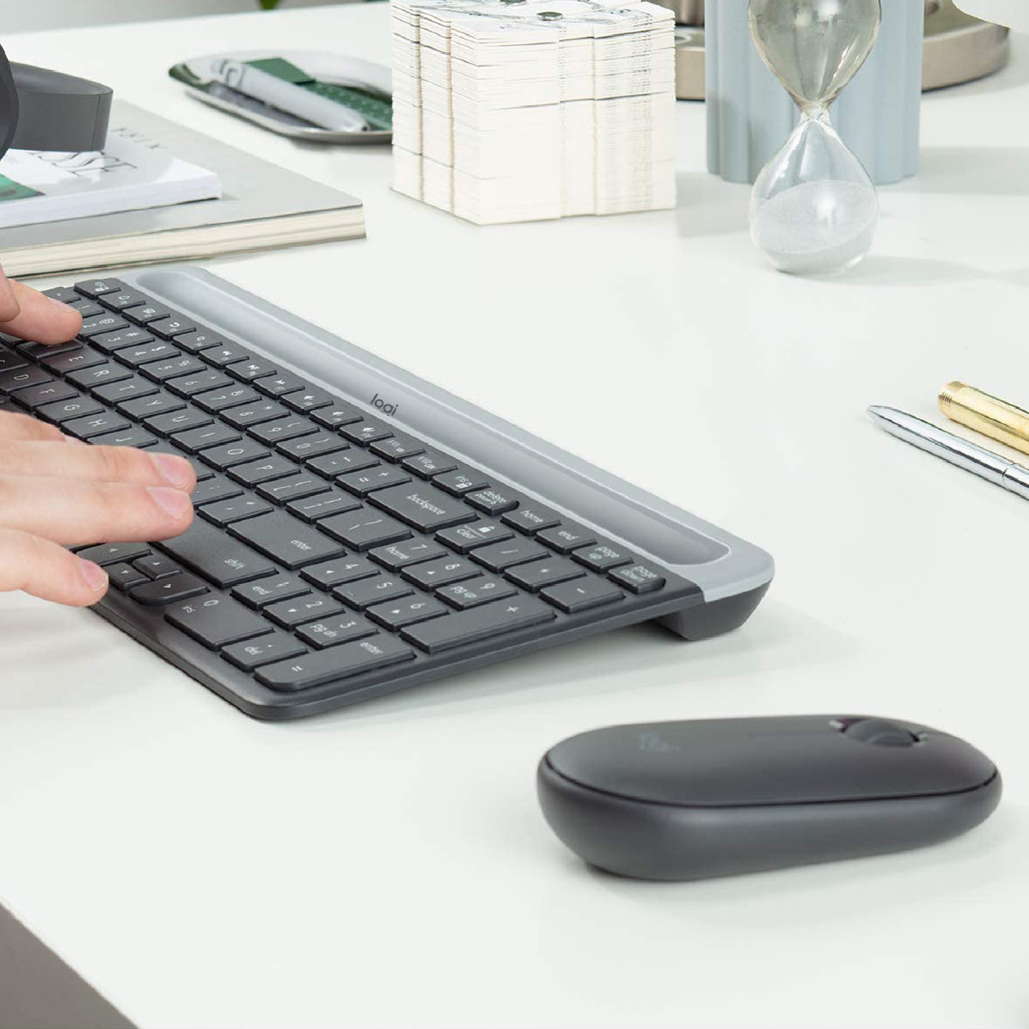 Die Hände einer Person liegen auf einer schwarzen Tastatur und einer schwarzen Maus auf einem weißen Schreibtisch. Es gibt einen Stift.