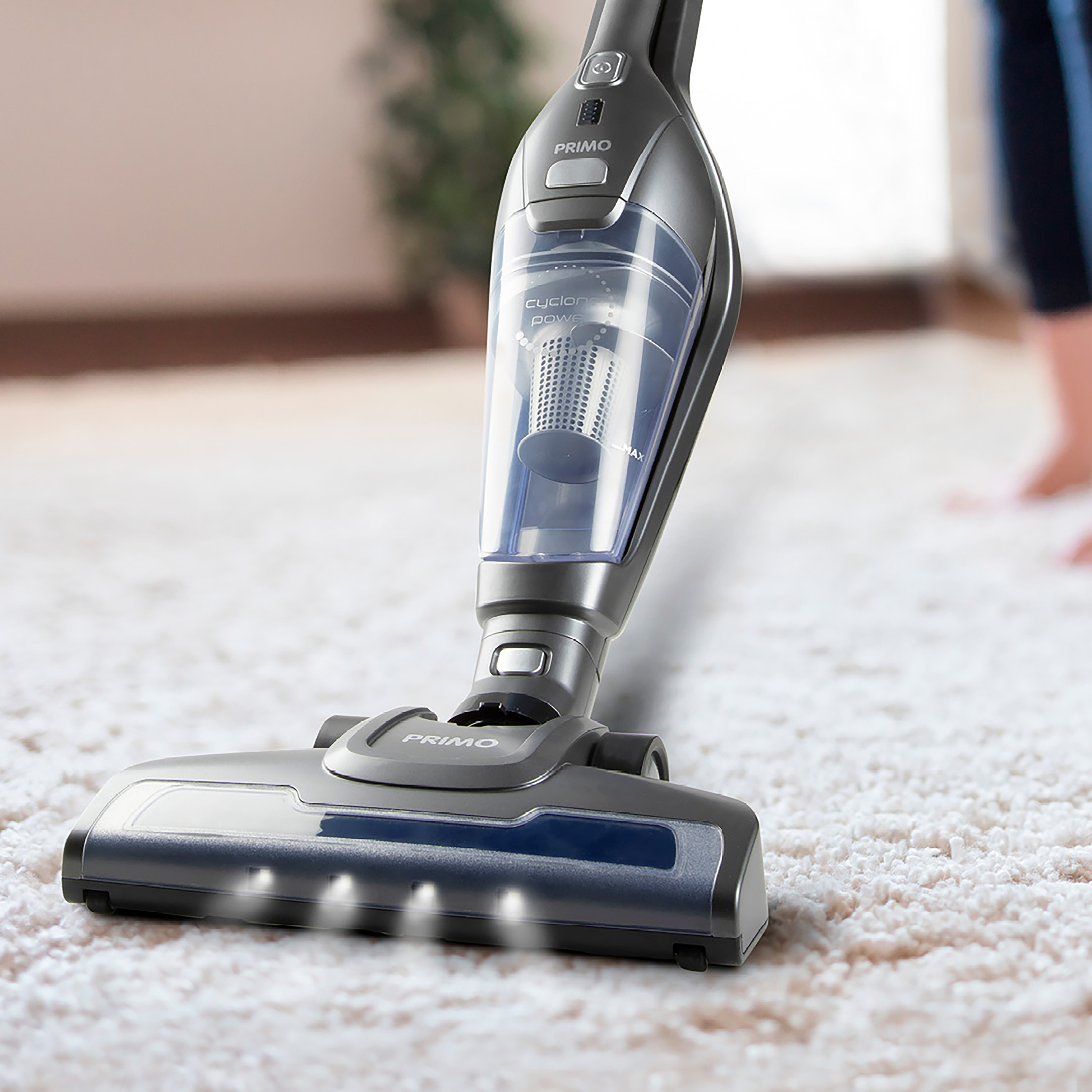 A person vacuuming a white rug with a gray and silver vacuum cleaner. The vacuum is on.