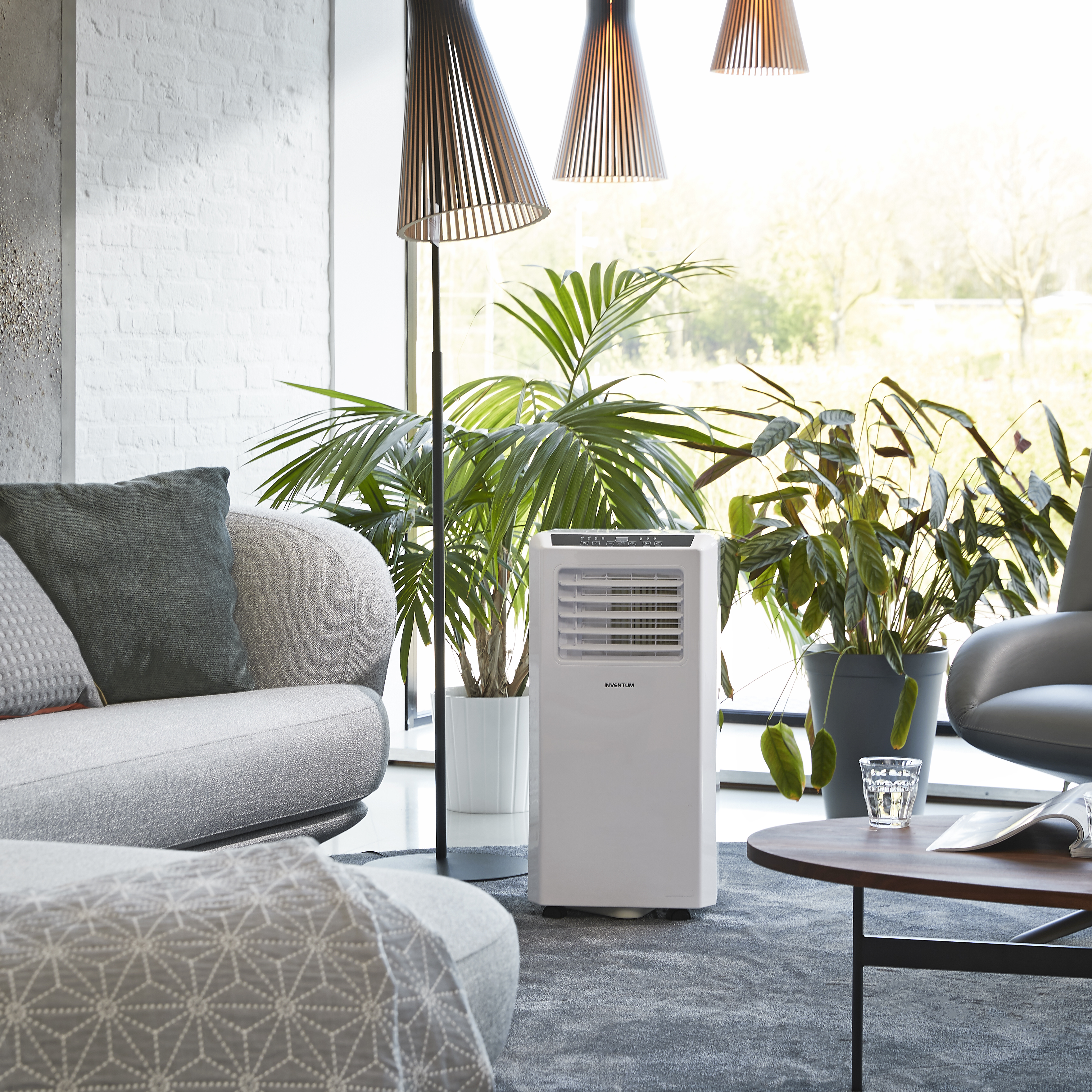 Witte draagbare airconditioner in een moderne woonkamer, met planten, bank en lampen.
