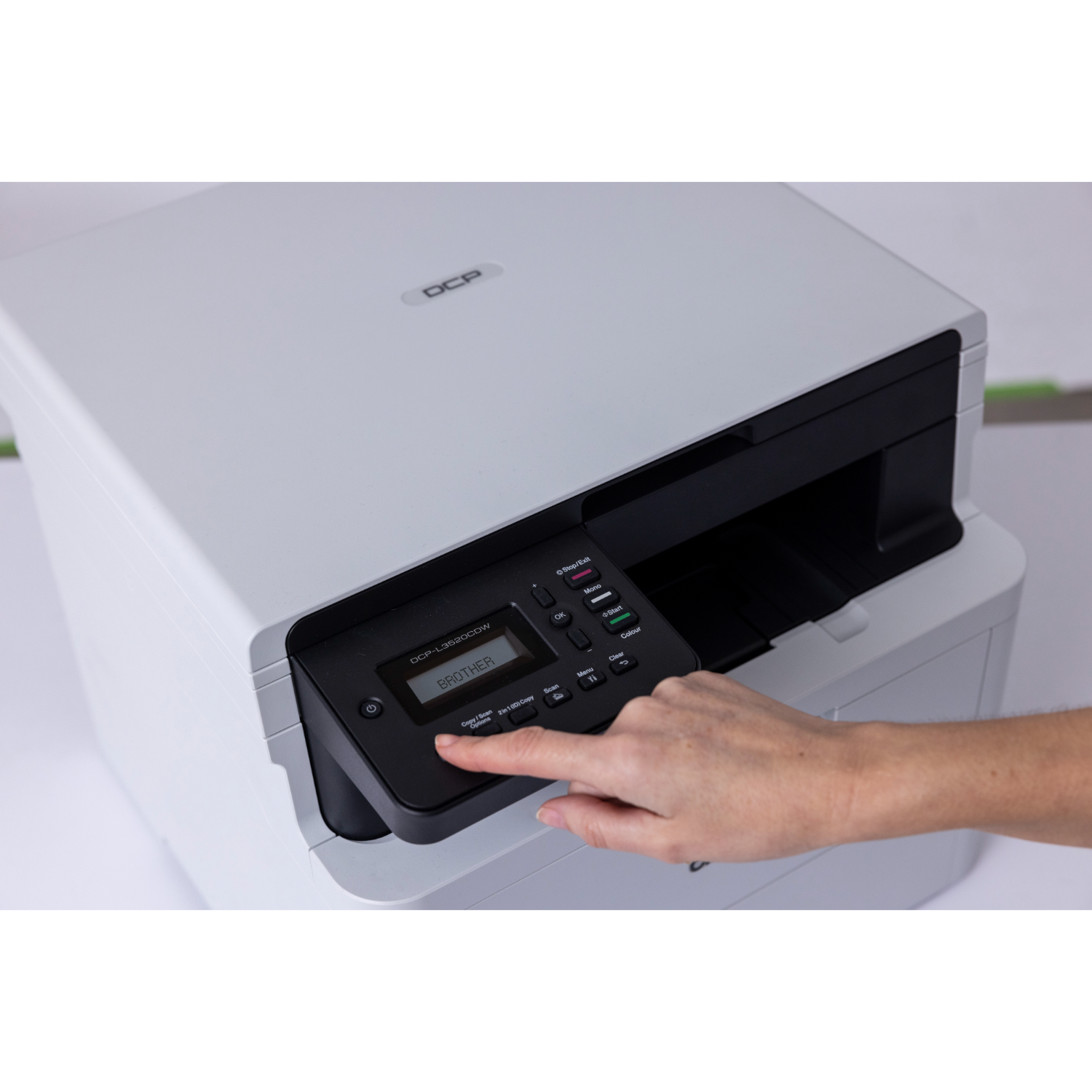 Ręka osoby naciskająca przycisk na drukarce Brother. Drukarka jest biało-czarna.