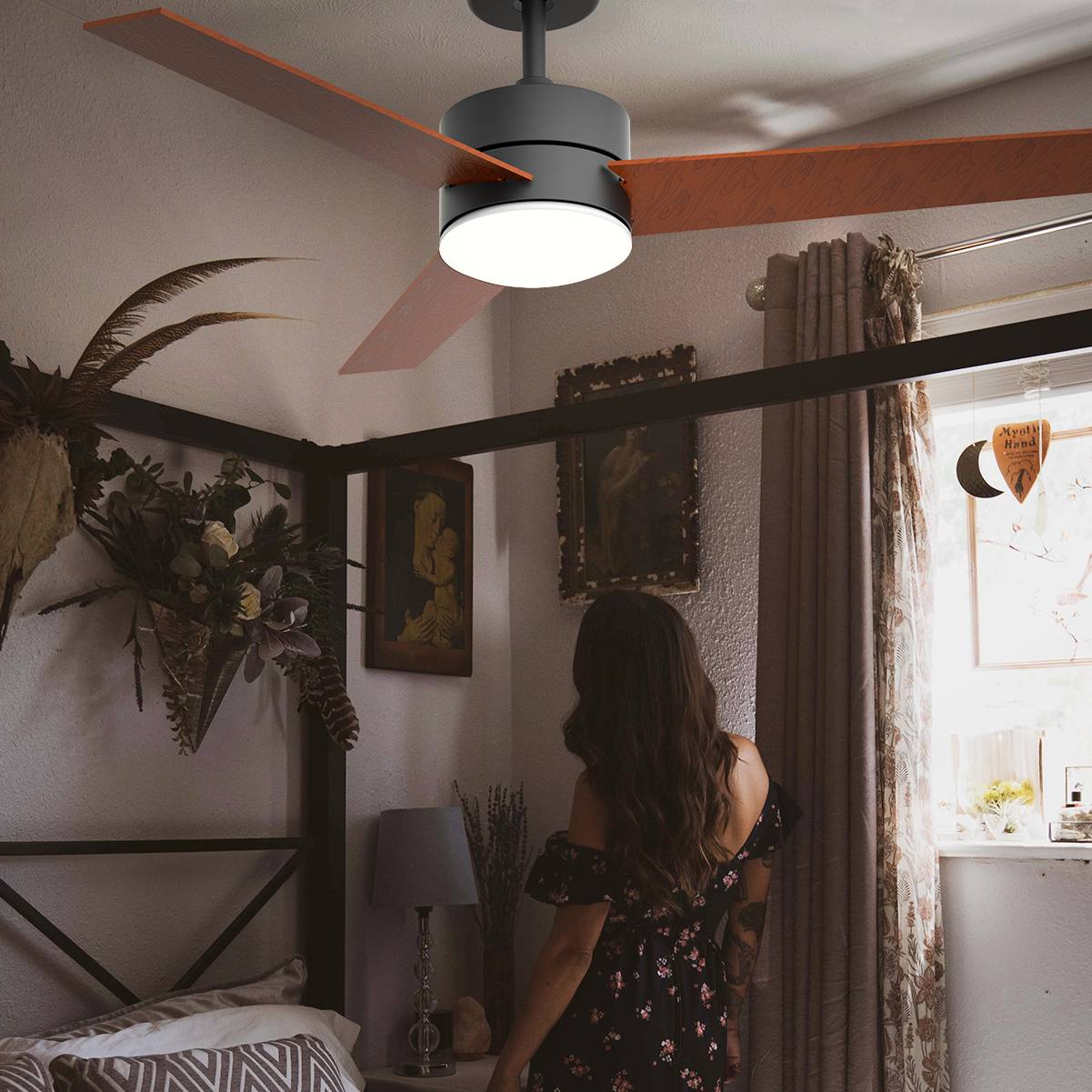 Donna guarda un ventilatore a soffitto con pale in legno. Stanza buia con letto.