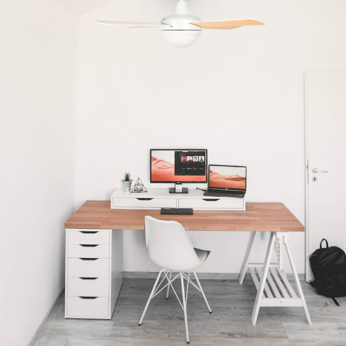 Uno spazio di lavoro moderno con scrivania, computer, laptop, sedia e ventilatore a soffitto.