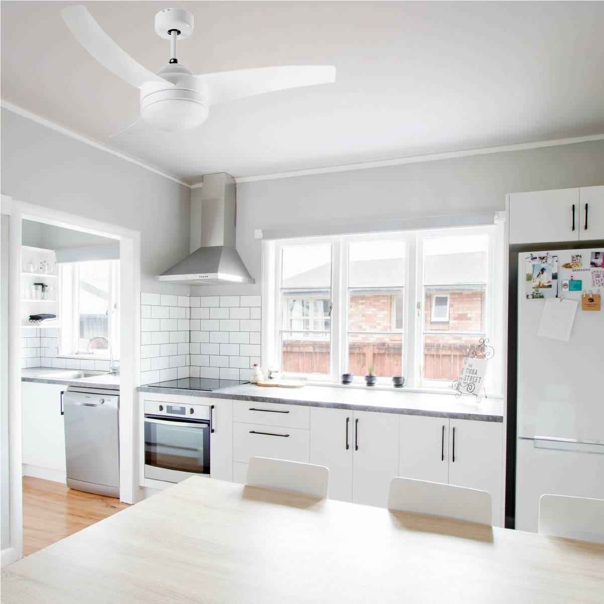 Cucina moderna con mobili bianchi, cappa in acciaio inox e ventilatore a soffitto.