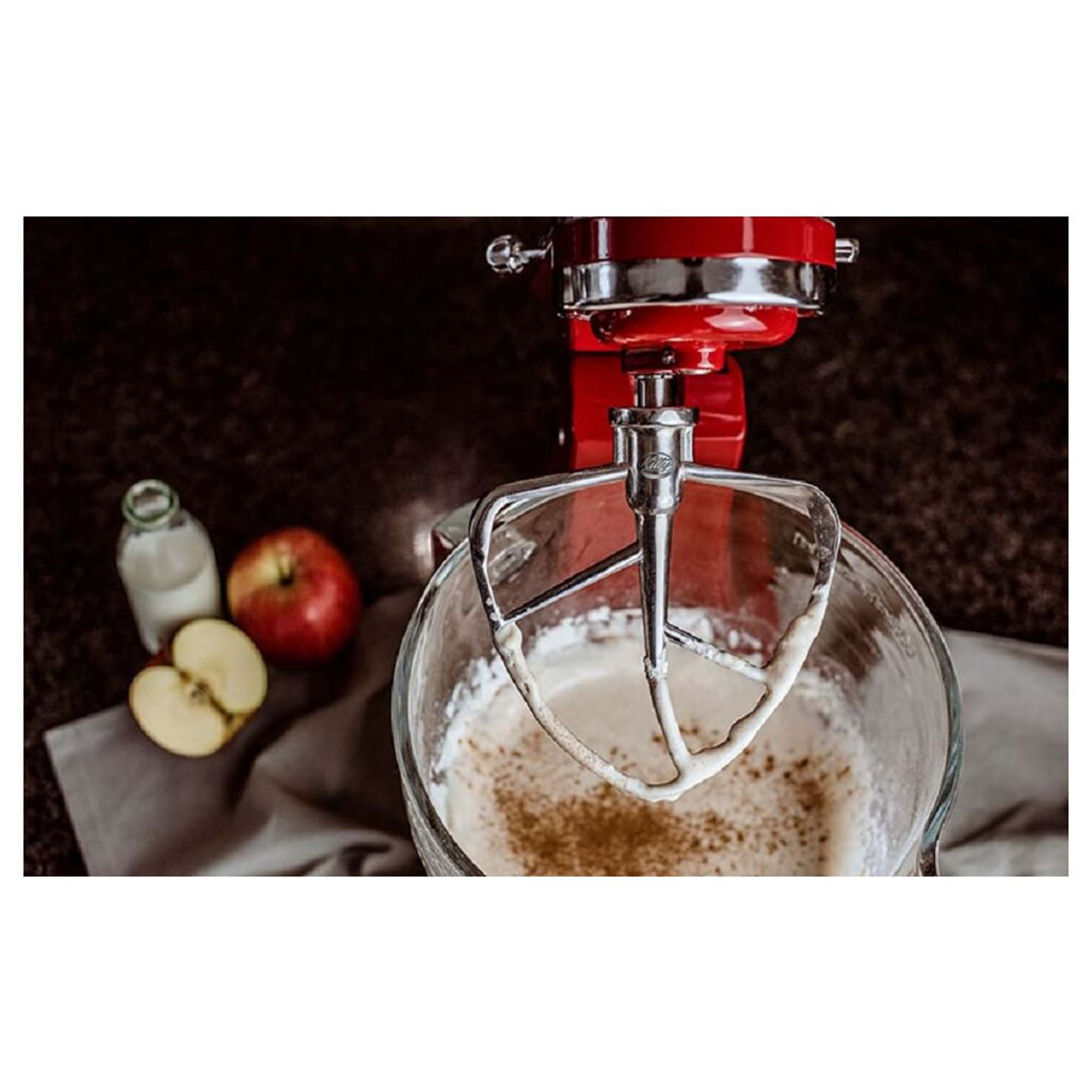 Roter Küchenmixer mit Glasschüssel, Milchflasche und Apfel auf dem Tisch.