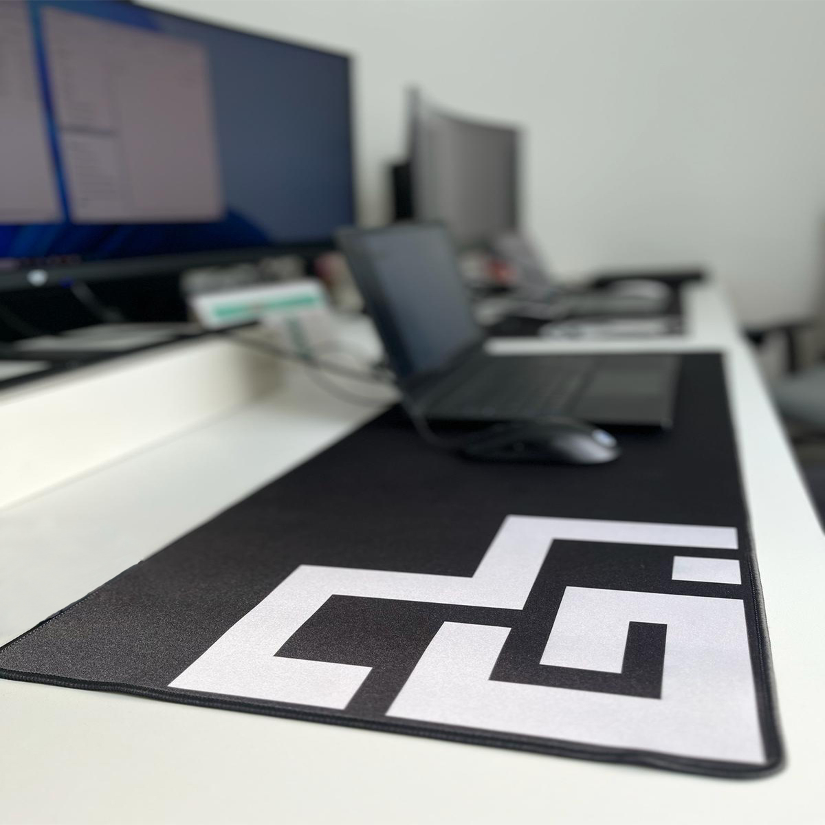 Ratón y portátil negros sobre una alfombrilla de escritorio con diseño en blanco y negro.