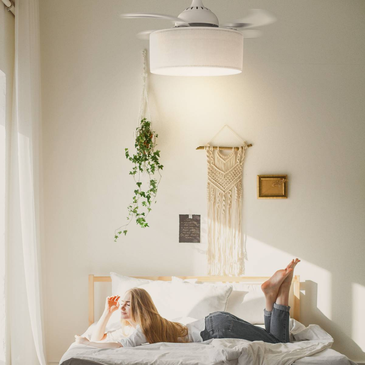 Una donna su un letto, con un ventilatore e piante appese. La stanza è bianca e luminosa.