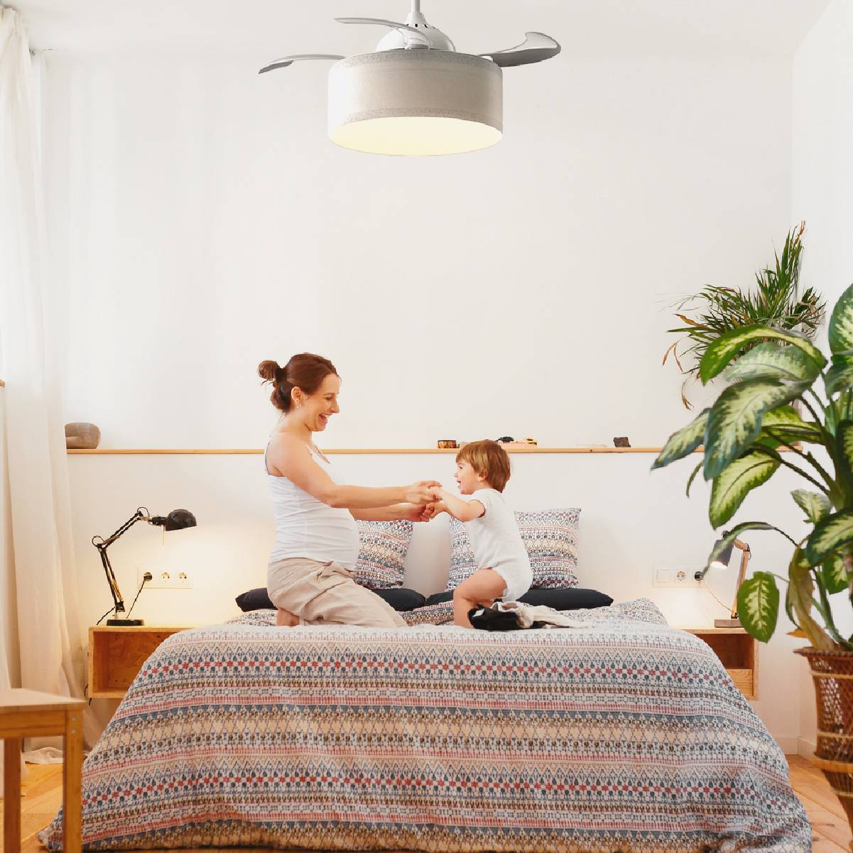 Donna e bambino sul letto, che giocano, luce dall'alto e piante.