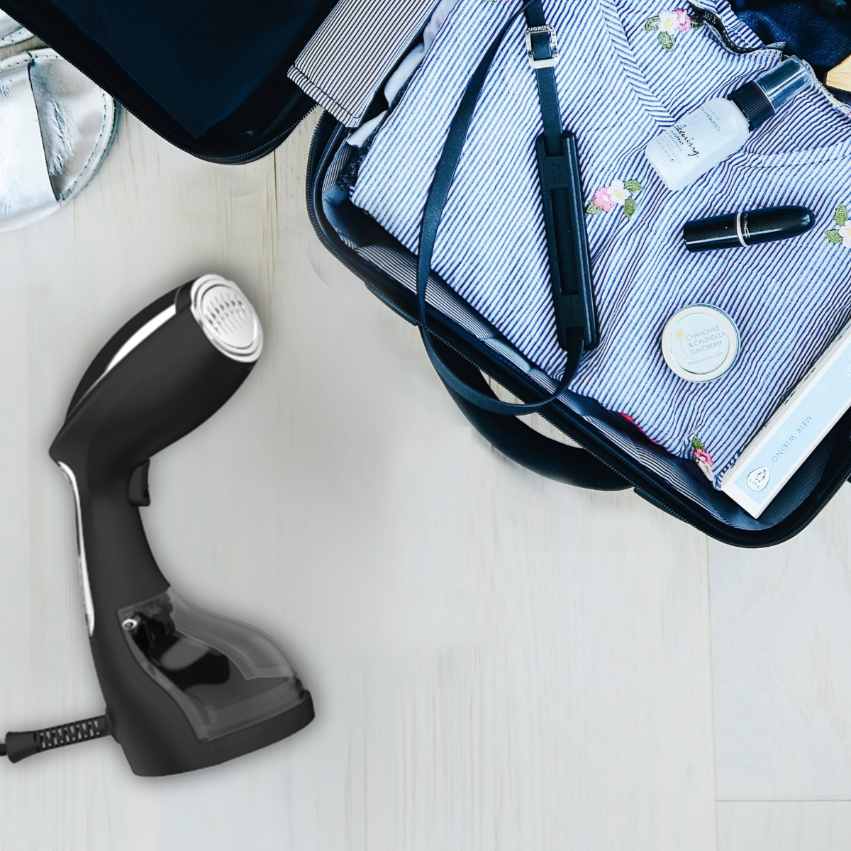 Zwarte kledingstomer, koffer en accessoires op een houten vloer.