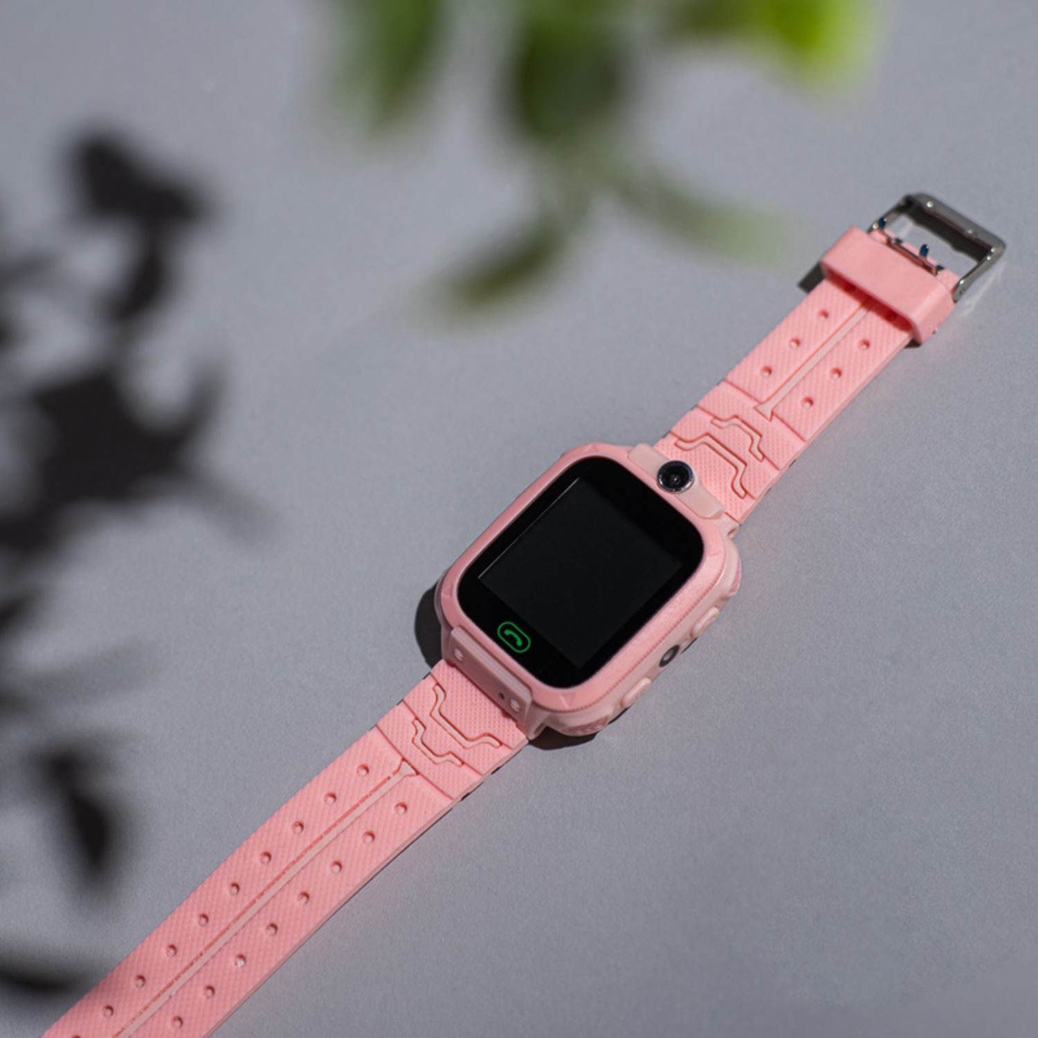 Eine rosa Smartwatch mit schwarzem Bildschirm und rosa Armband liegt auf grauem Untergrund.