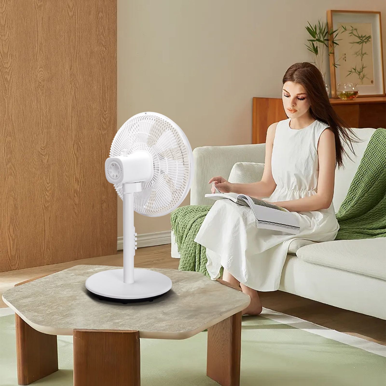 Una mujer leyendo un libro junto a un ventilador blanco sobre una mesa de madera.
