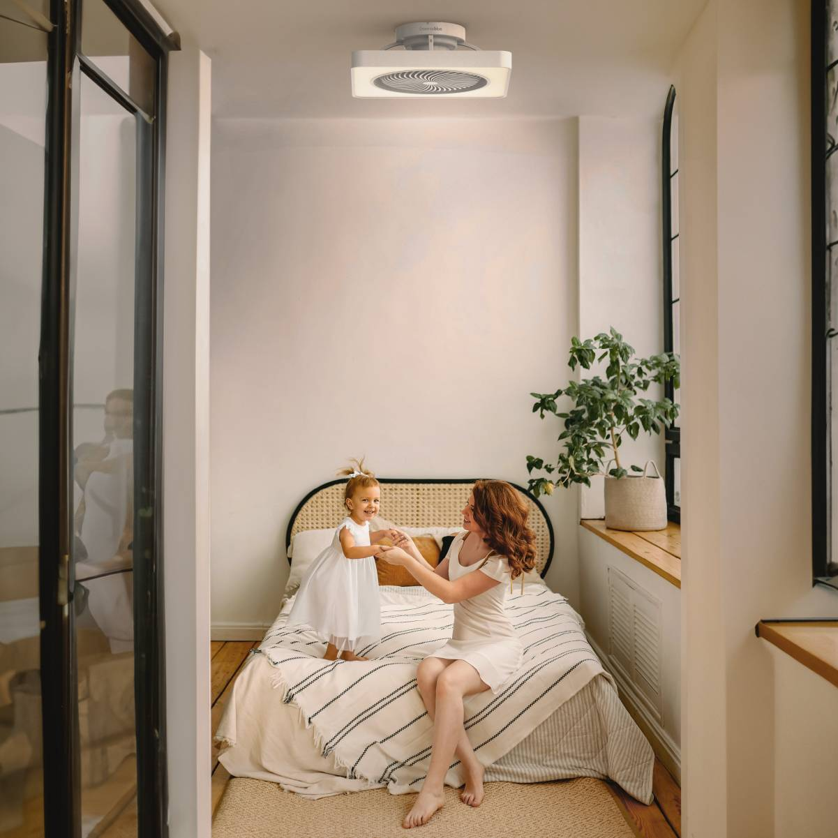 Una donna e una bambina in una stanza con un letto e un ventilatore a soffitto.