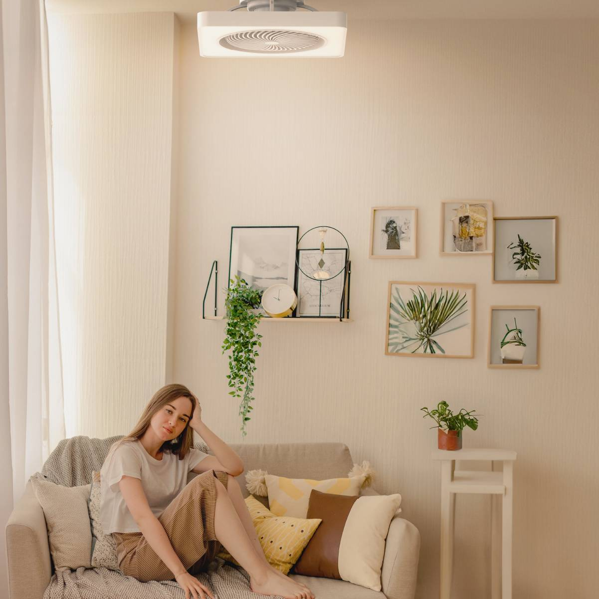 Una donna su un divano sotto un ventilatore a soffitto, con arte sulla parete.