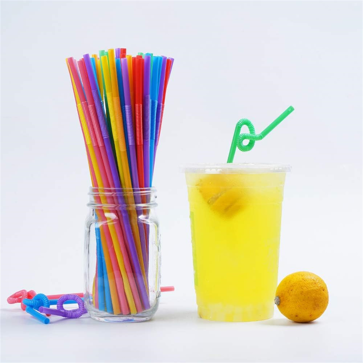 Glas mit bunten Strohhalmen, ein Glas mit gelbem Getränk und eine Zitrone.