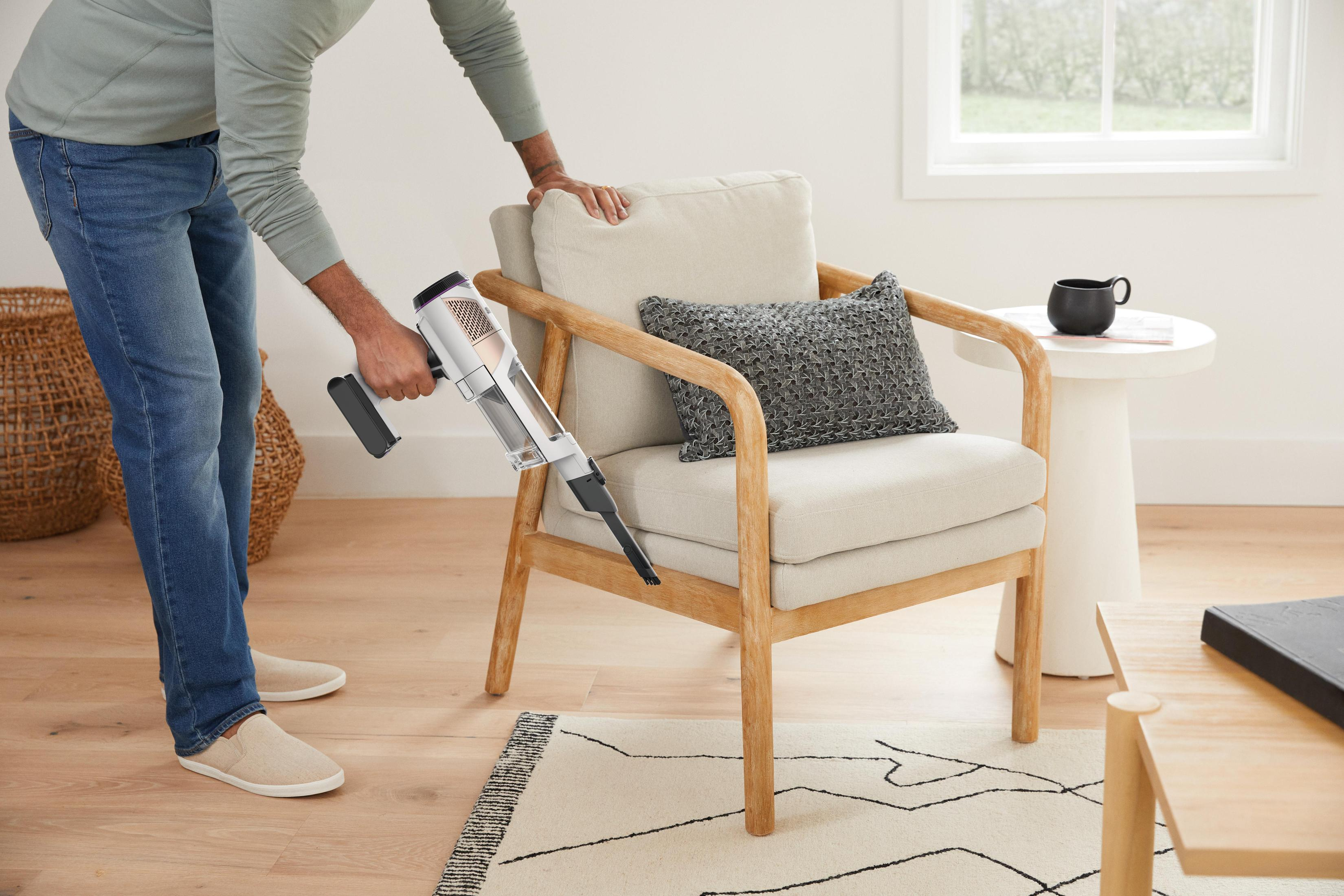 A person is vacuuming a chair using a handheld vacuum cleaner in a living room.