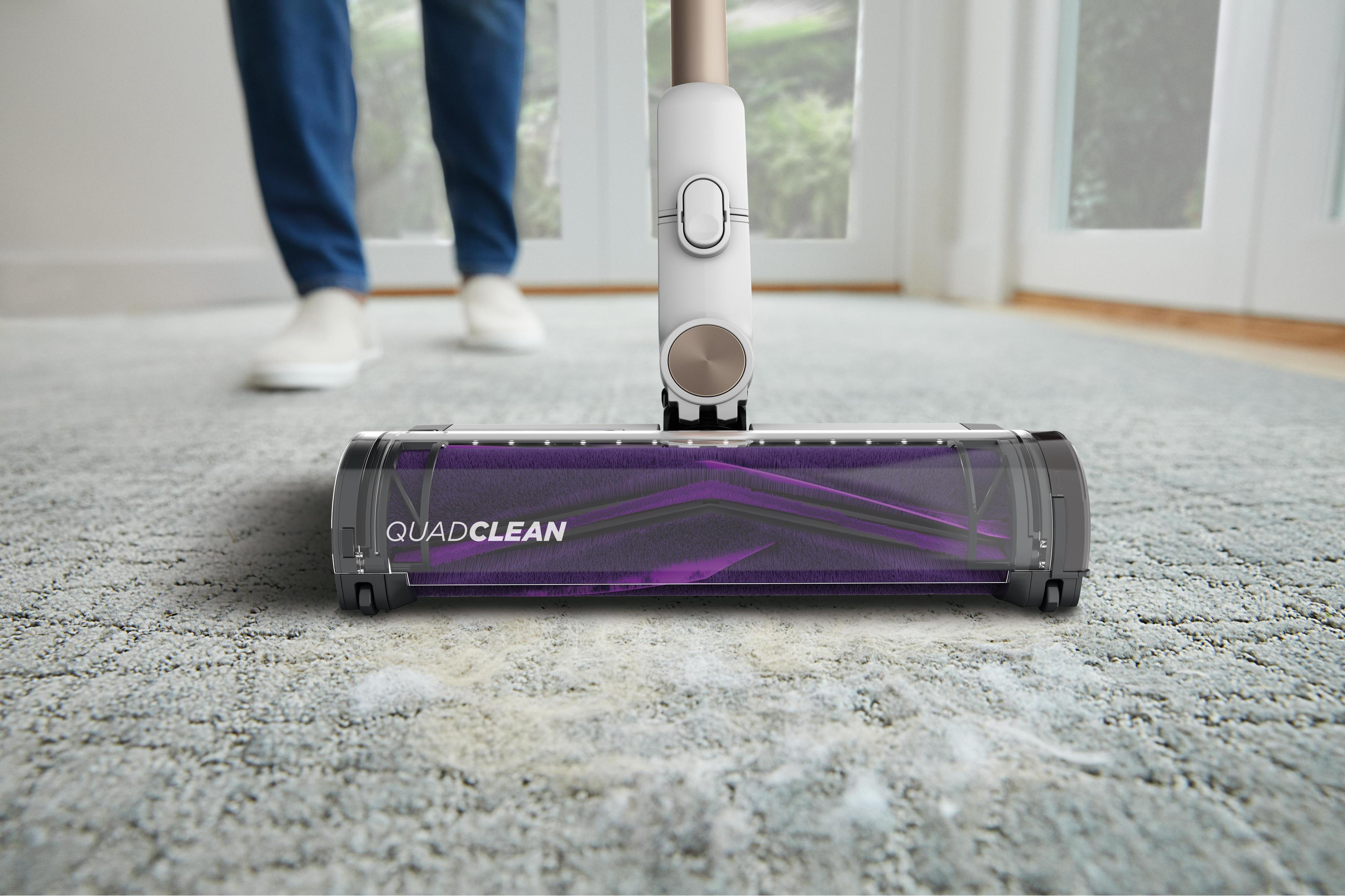 Person vacuuming a light gray carpet. The vacuum cleaner head is in the foreground.