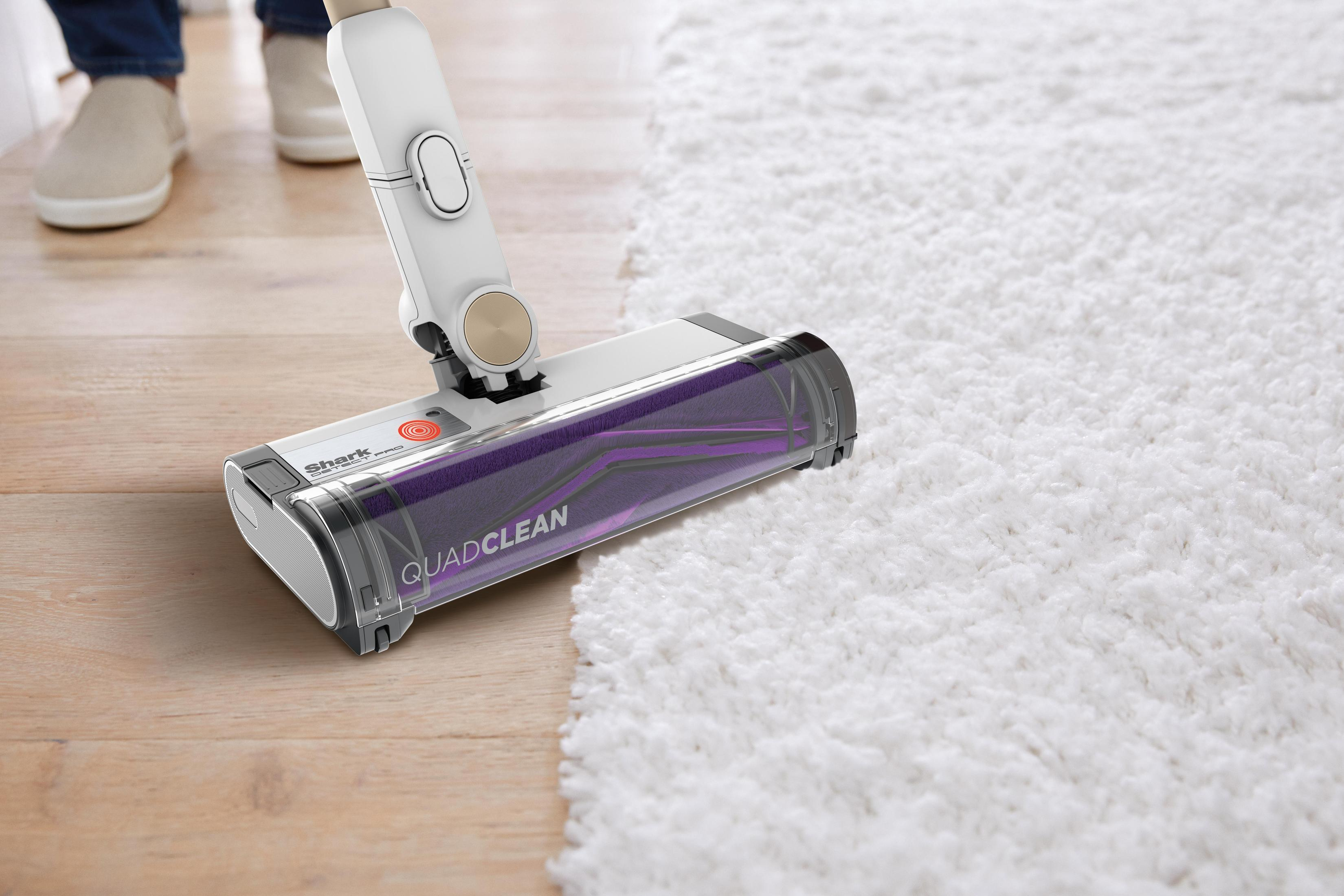 Vacuum head on wood floor, cleaning white fluffy rug. Part of vacuum visible.