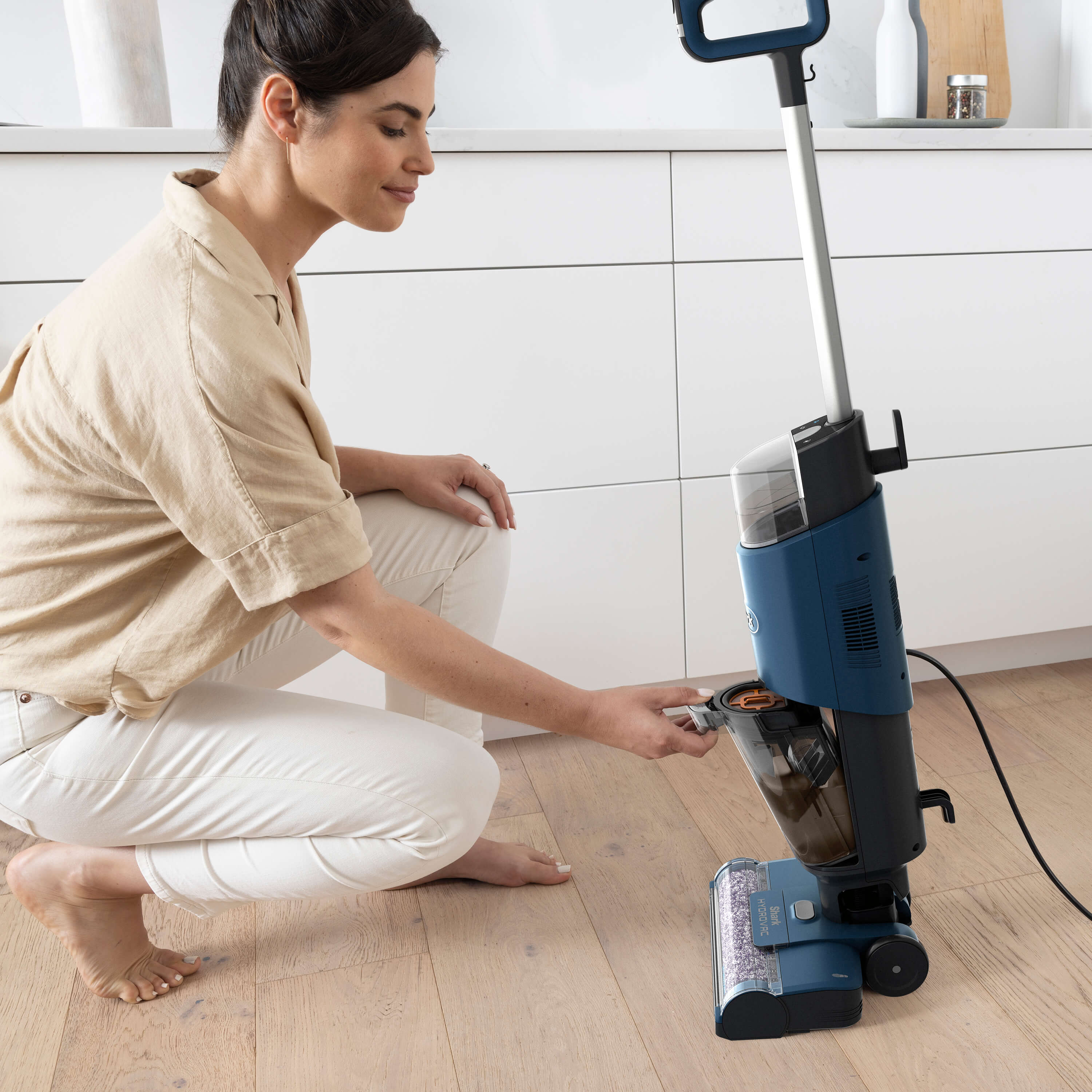 A woman using a cleaning machine. She is cleaning the floor in a modern kitchen.