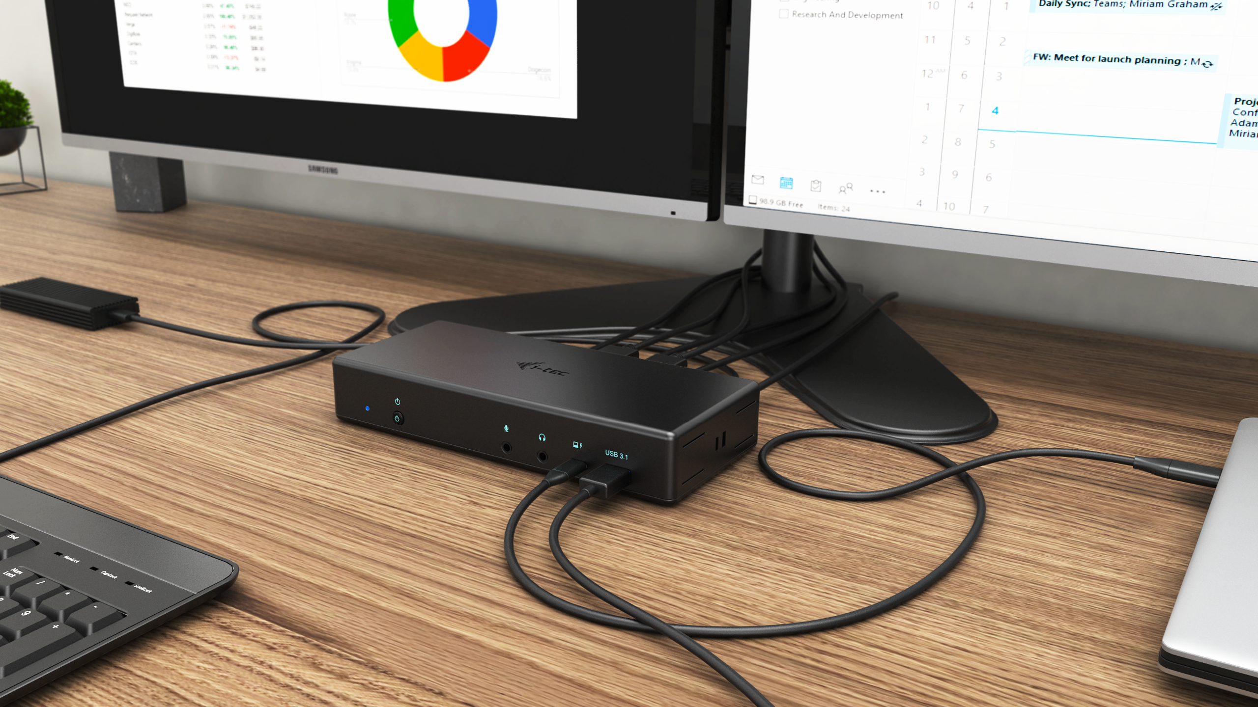 Una scrivania in legno con una docking station, computer, monitor, tastiera e cavi.