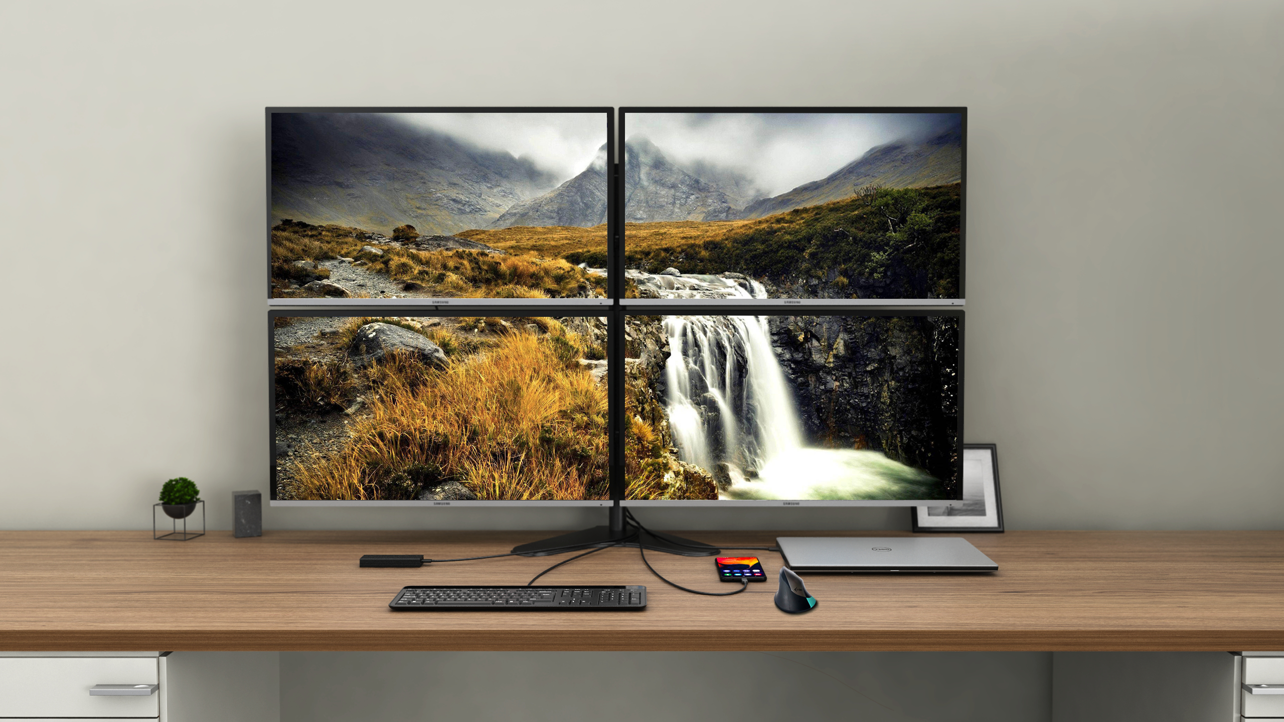 Configurazione multi-monitor su una scrivania in legno che mostra una cascata, con periferiche e laptop.