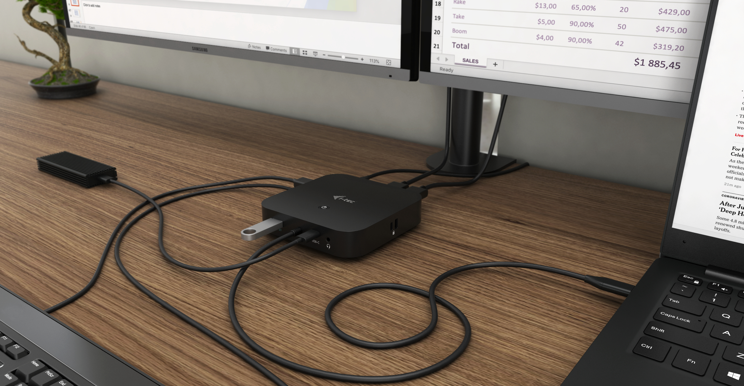 Desk setup with two monitors, a hub, and a laptop. A small plant is on the desk. Wires are visible.