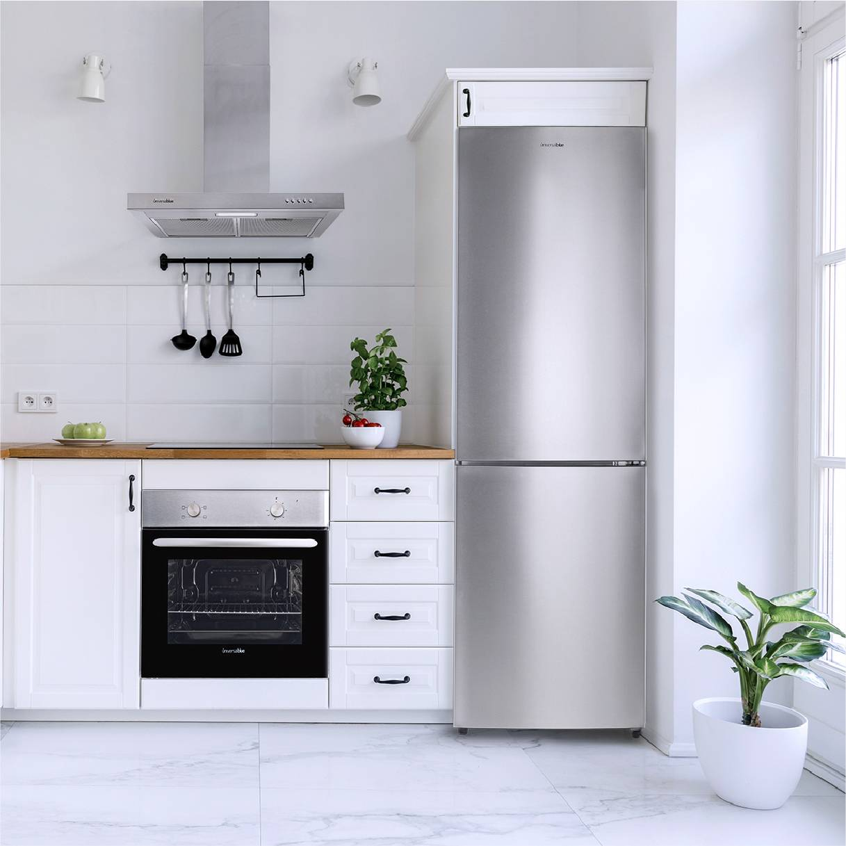 Cocina con armarios blancos, nevera y horno de acero inoxidable. Encimera de madera, plantas y campana extractora.