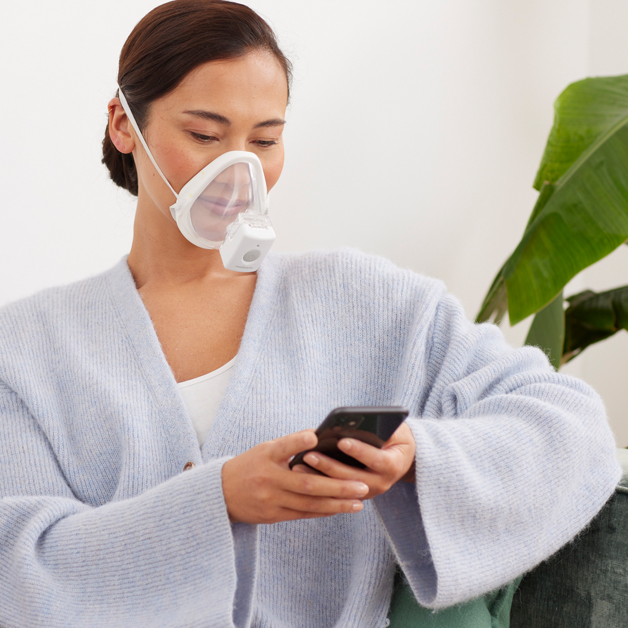 A woman wearing a face mask connected to a device, looking at her smartphone.