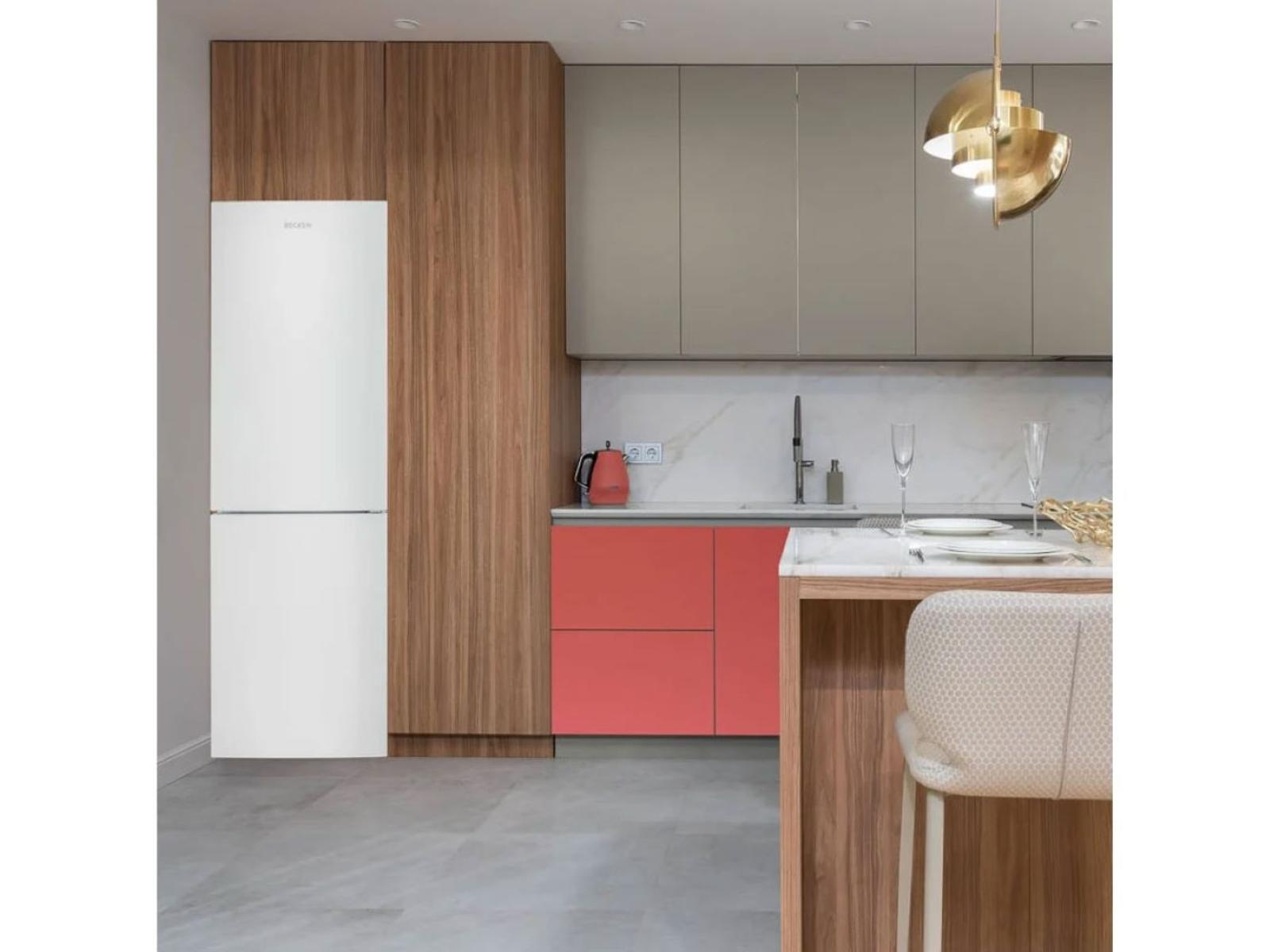 Un refrigerador blanco en una cocina con gabinetes de madera y un acento rojo.