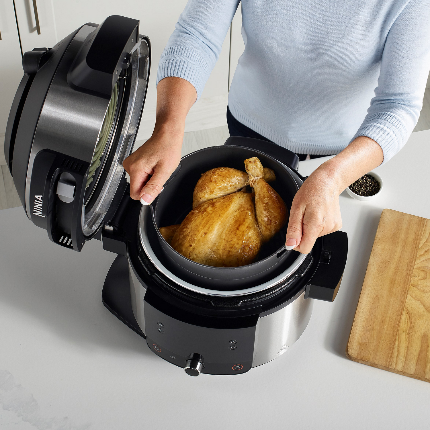 Frau öffnet eine schwarze Heißluftfritteuse mit einem ganzen Hähnchen darin.