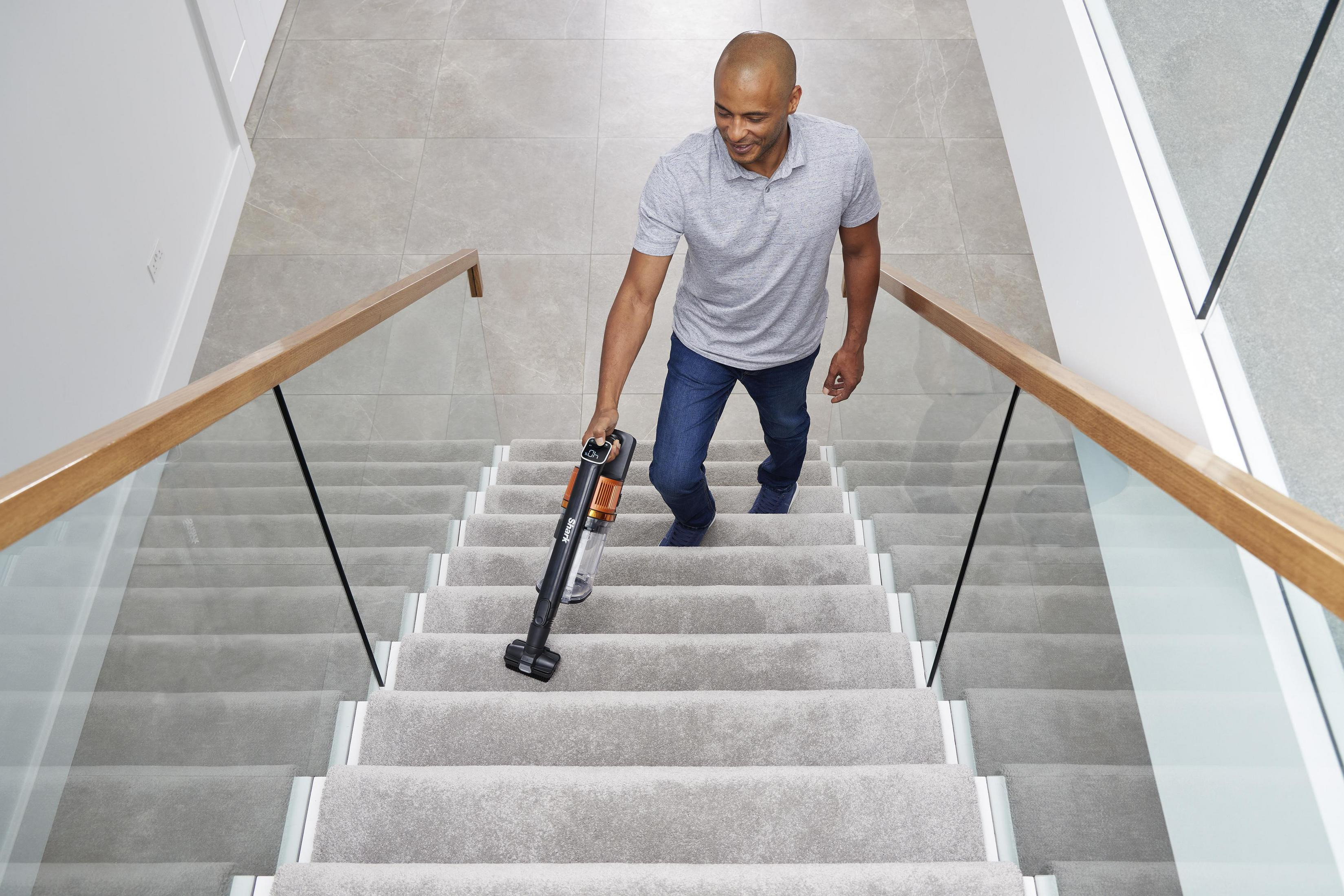 Hombre aspira escaleras alfombradas con una aspiradora negra y naranja.