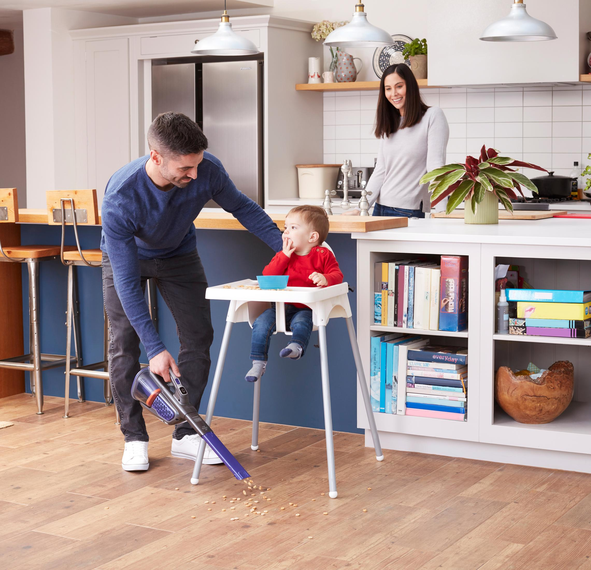 Rodzina w kuchni: tata odkurza, dziecko w krzesełku do karmienia, kobieta.
