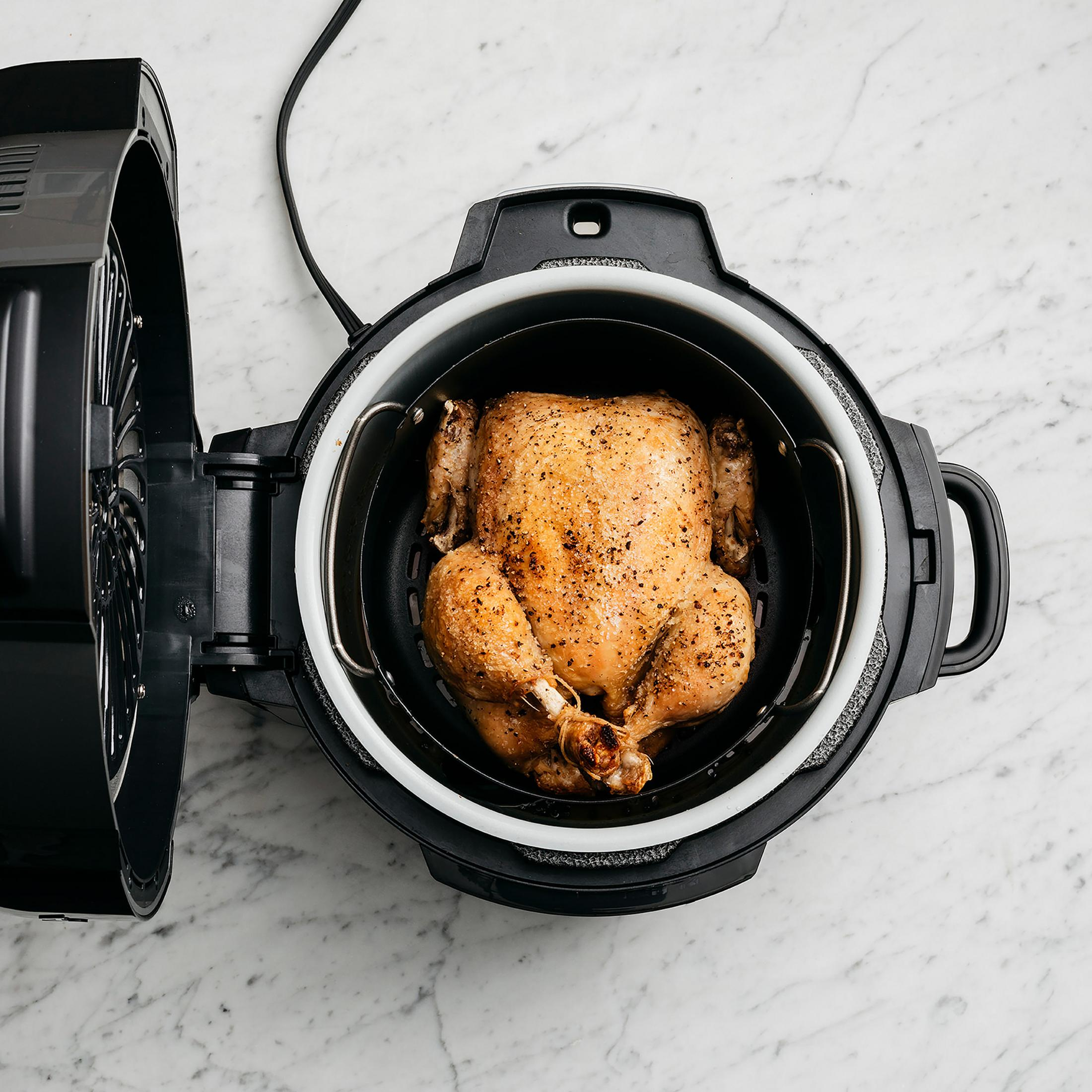 Pollo arrosto intero in una friggitrice ad aria nera. Coperchio aperto. Piano di lavoro in marmo.